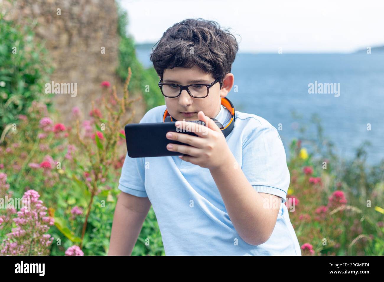 Porträt eines 11-jährigen Jungen mit Brille, der sich draußen auf dem Smartphone ansieht, horizontal Stockfoto