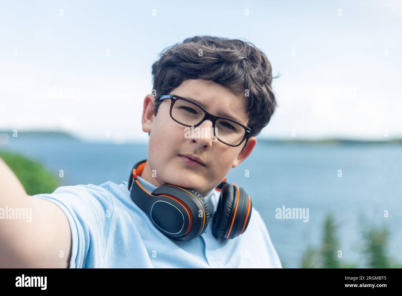 Porträt eines 11-jährigen Jungen mit Brille und kabellosen Kopfhörern, Selfie, Meer im Hintergrund Stockfoto