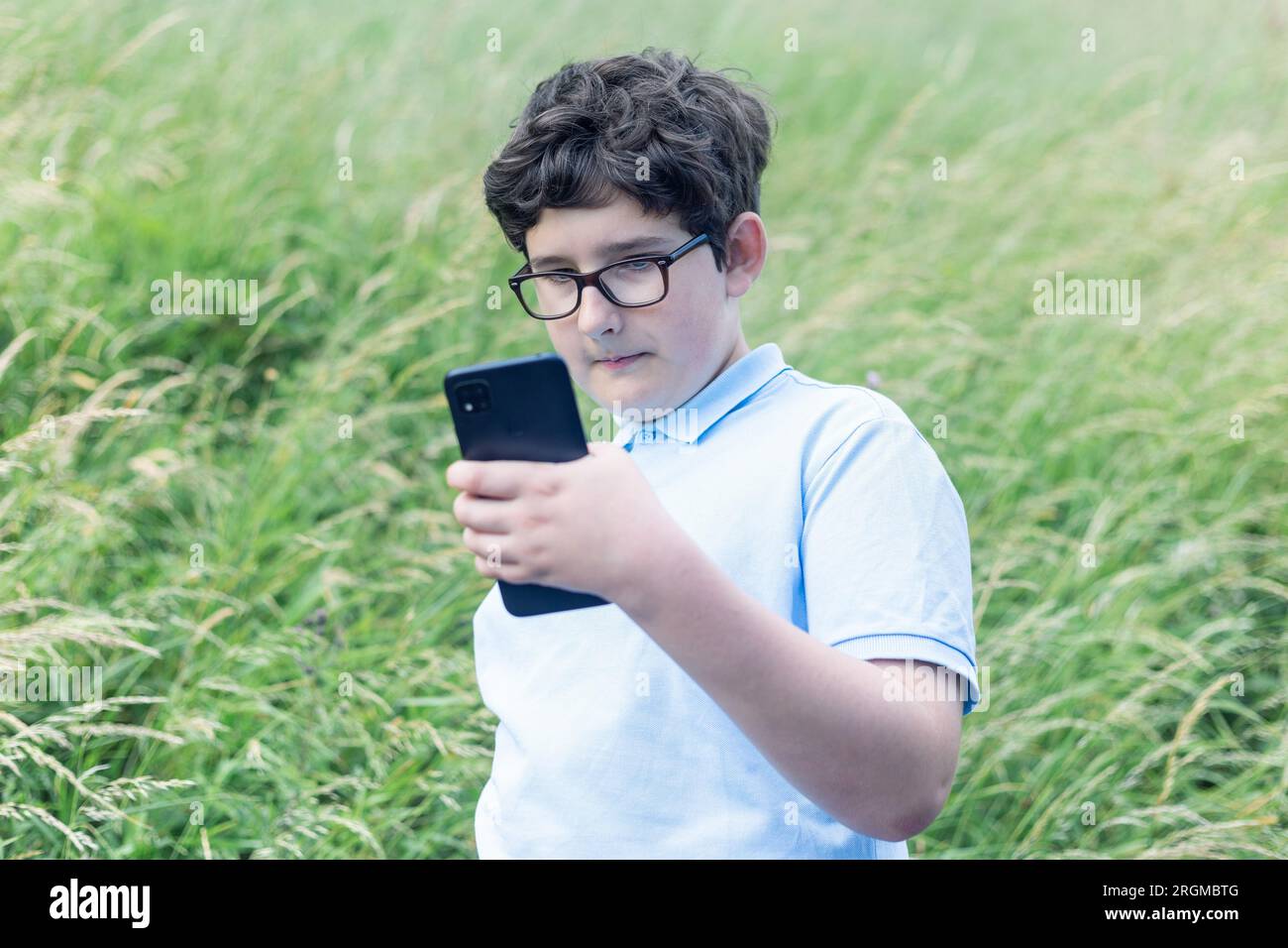 Porträt eines 11-jährigen Jungen mit Brille, der im Freien auf ein Smartphone schaut, horizontal Stockfoto