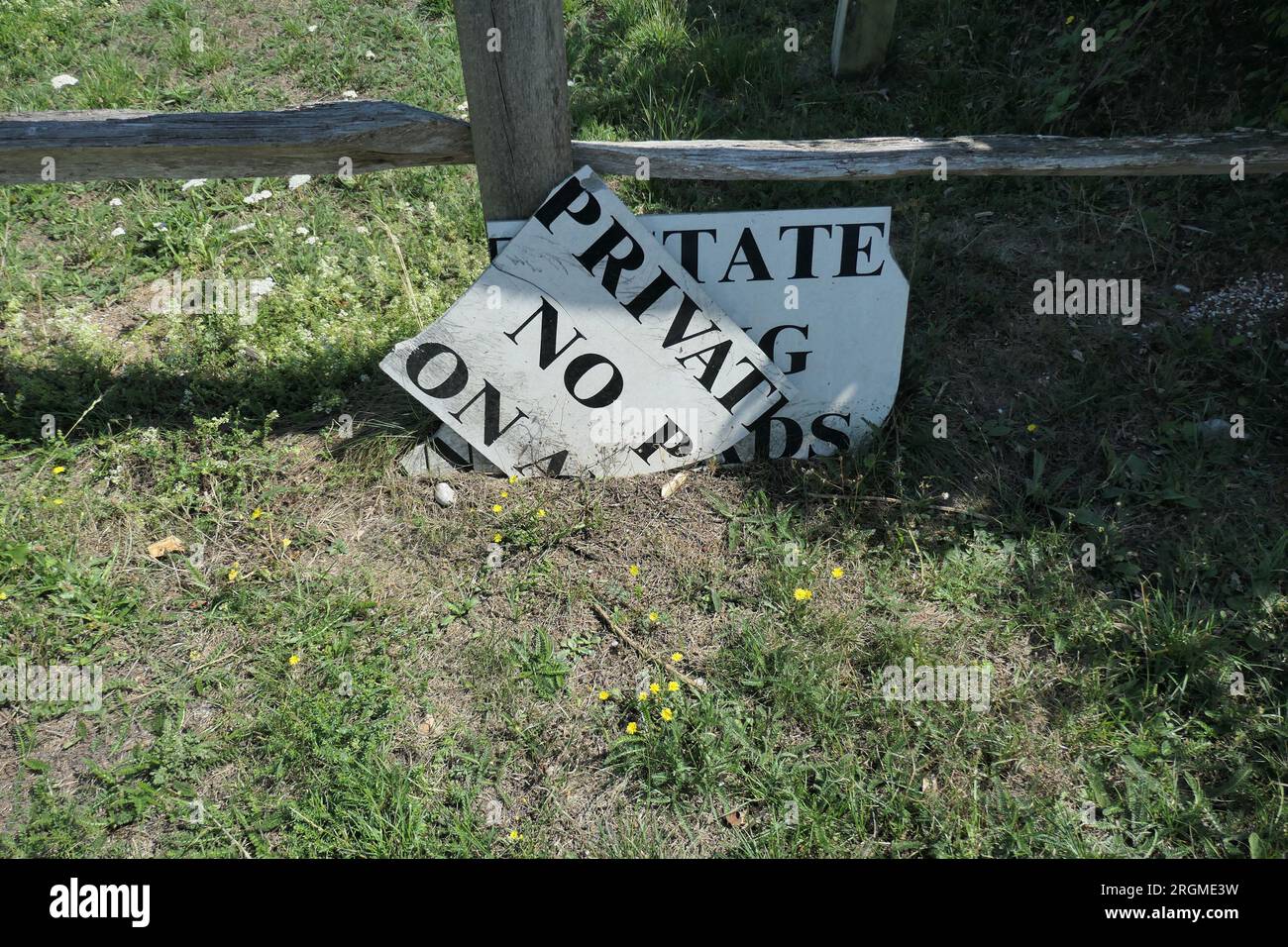 Nahaufnahme eines kaputten Privatgrundstücksschilds, das im grünen Gras vor einem Grenzzaun liegt. Stockfoto