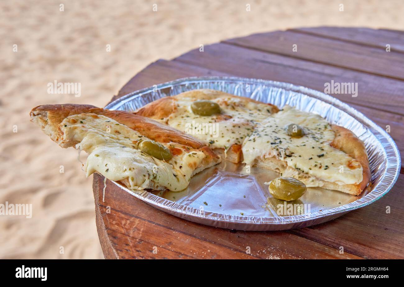 Leckere Pizzaschneiden am Strand, mit Mozzarella und Oliven auf einem Holztisch im Sommer Stockfoto