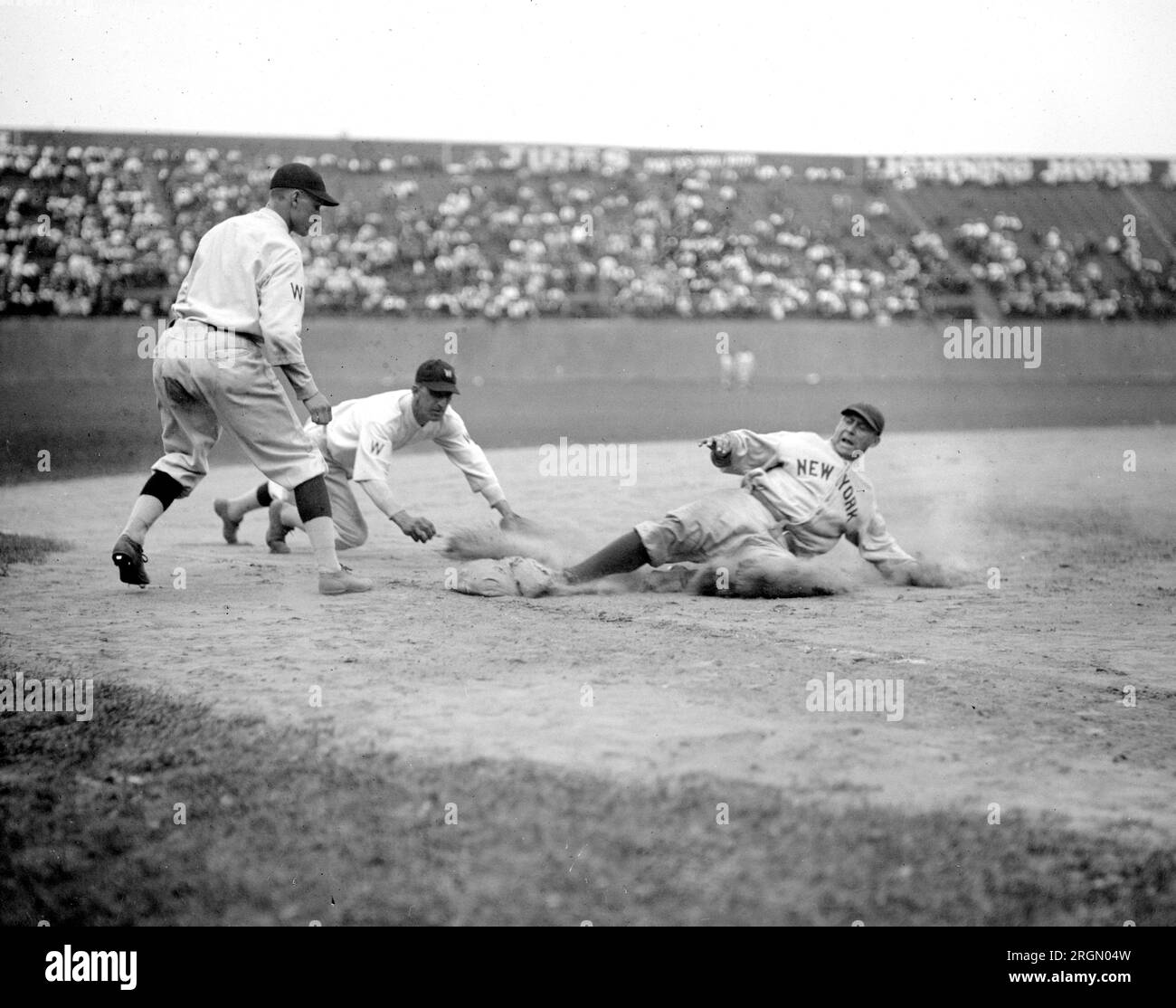 Der Yankees-Fänger Wally Schang rutscht im zweiten Spiel sicher in die 3. Base. Senators 3. Baseman ist Ossie Bluege und der Pitcher, der das Spiel unterstützt, ist Firpo Marberry. Senatoren gewannen 2. Spiel 7-2 ca. 5. Juli 1924 Stockfoto