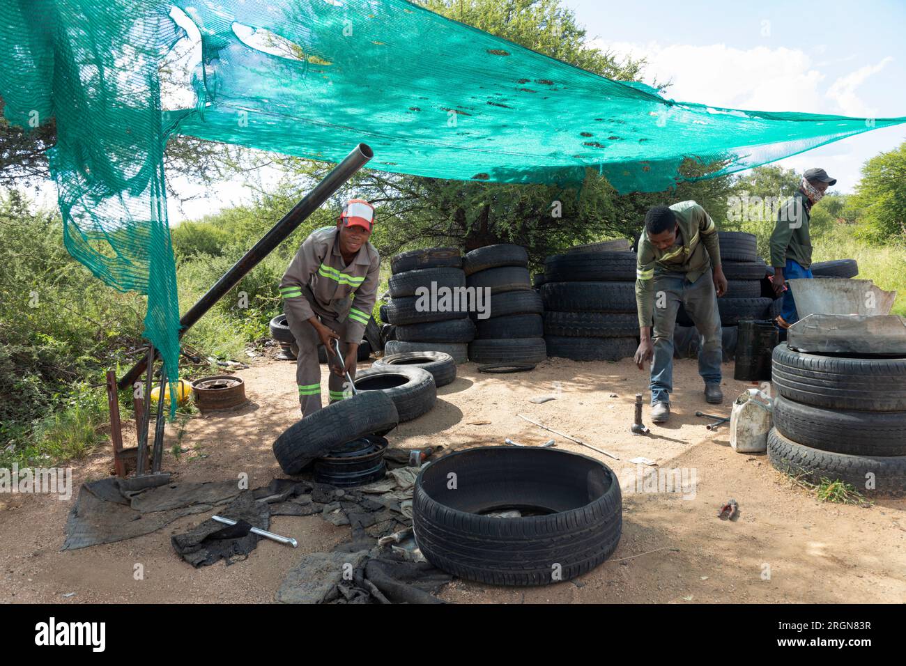 afroamerikanische Straßenräuber, die Reifen reparieren und aufblasen, um ihren Lebensunterhalt zu verdienen, ein Team von Arbeitern in Arbeitskleidung Stockfoto
