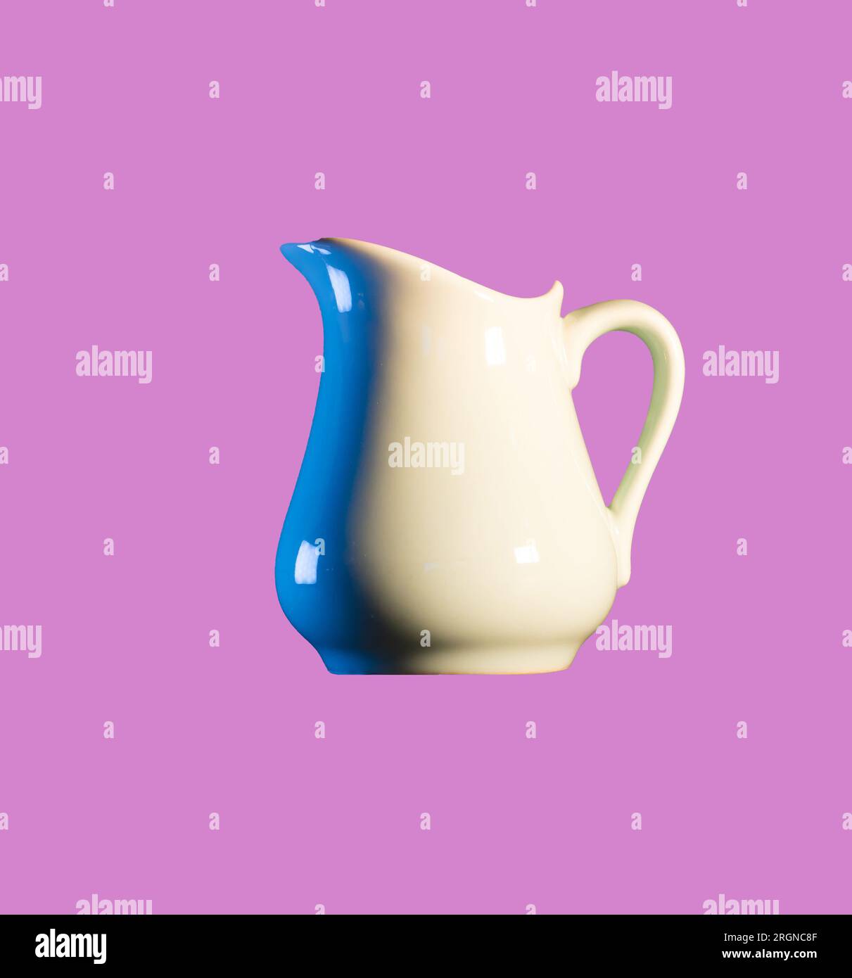 Ein weißer Keramik-Milchkrug, der blaues Licht reflektiert, isoliert auf pinkfarbenem Hintergrund Stockfoto