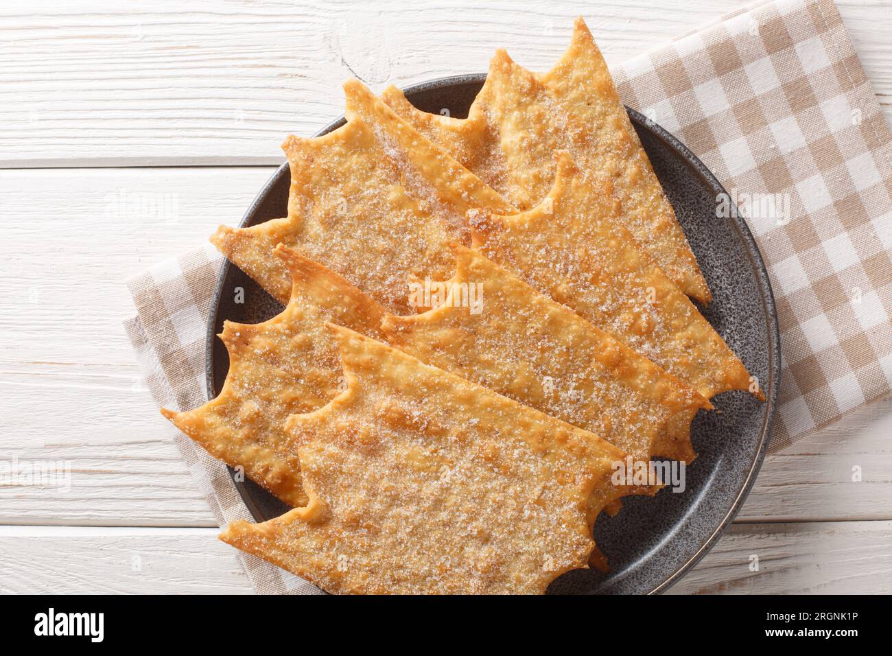 Französische süße Oreillette Karneval-Fritters, die auf dem Teller auf dem Holztisch zusammengelegt werden. Horizontale Draufsicht von oben Stockfoto