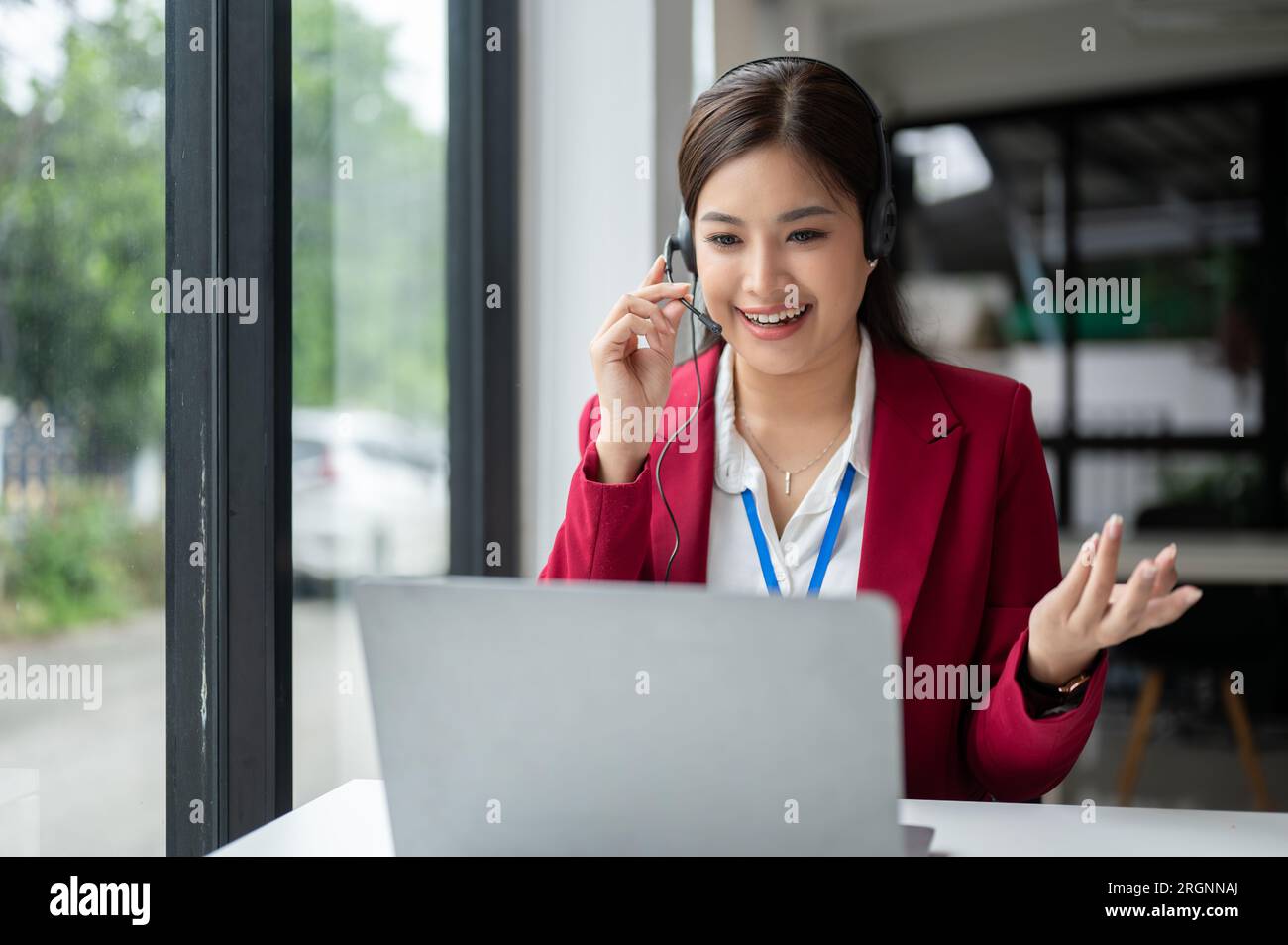 Eine zuversichtliche und zufriedene asiatische Kundendienstmitarbeiterin oder Callcenter-Agentin spricht und berät einen Kunden telefonisch oder Stockfoto