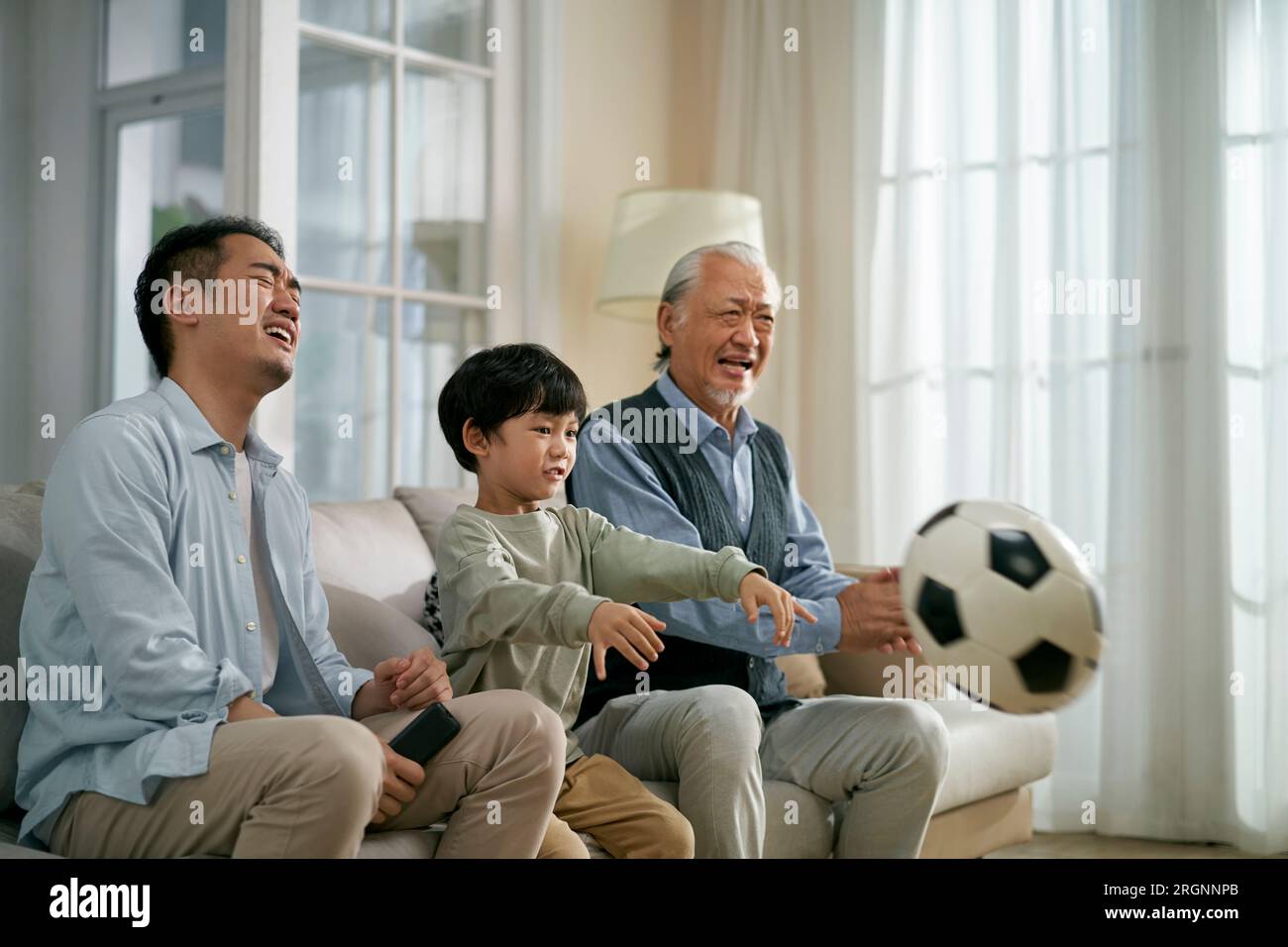 asiatischer Vater Großvater, der zu Hause auf der Couch saß und wütend und frustriert wurde, während er zusammen im Fernsehen Live-Übertragungen des Fußballspiels sah Stockfoto