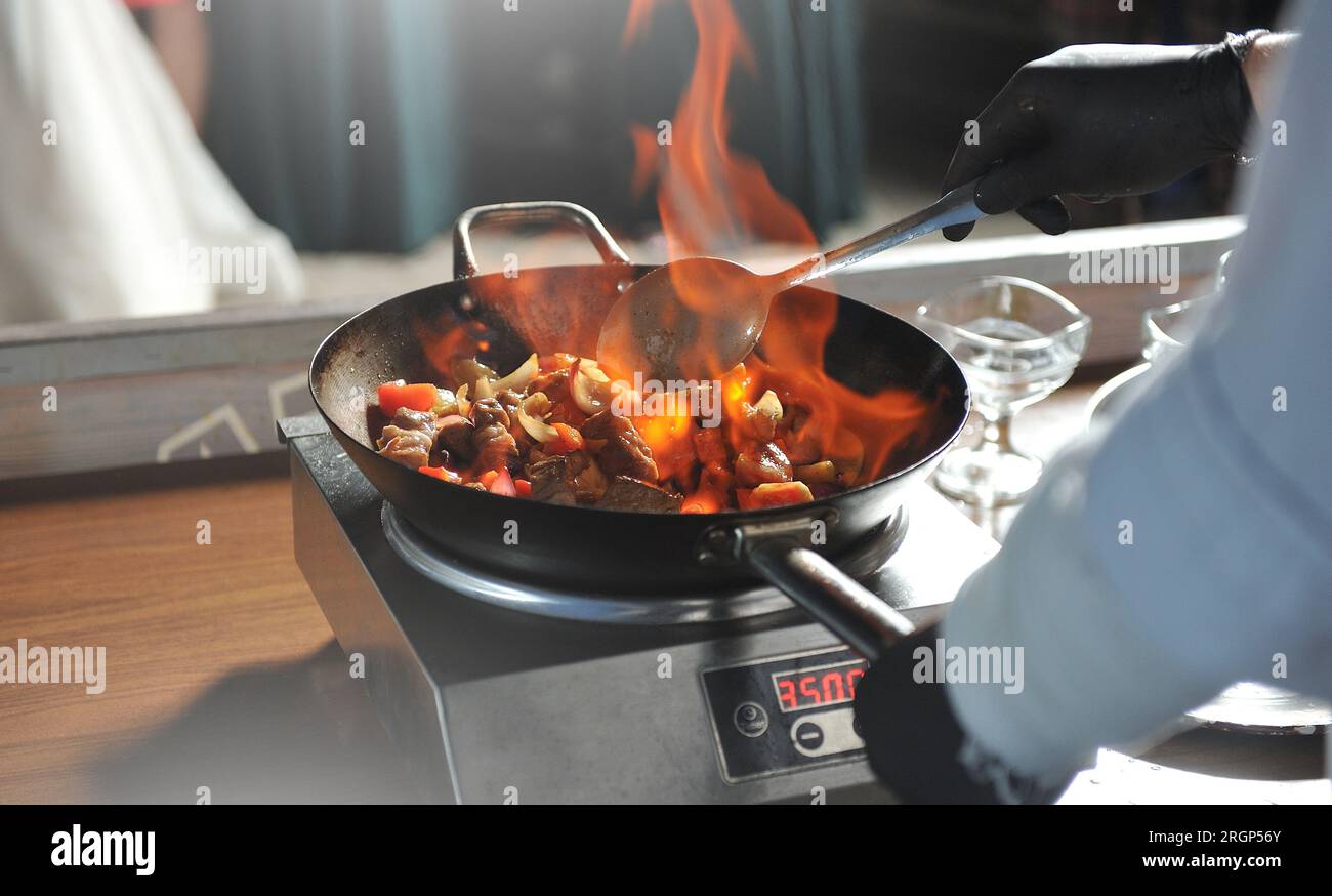 Ein Koch rührt Speisen in einer Pfanne mit Feuer auf einer Kochshow Stockfoto