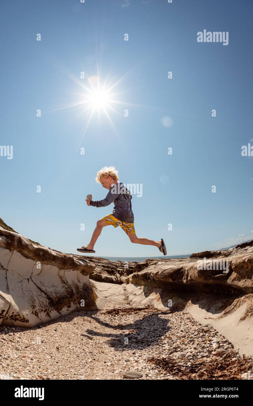 Aktives Kind, das an sonnigen Tagen an der felsigen Küste springt Stockfoto