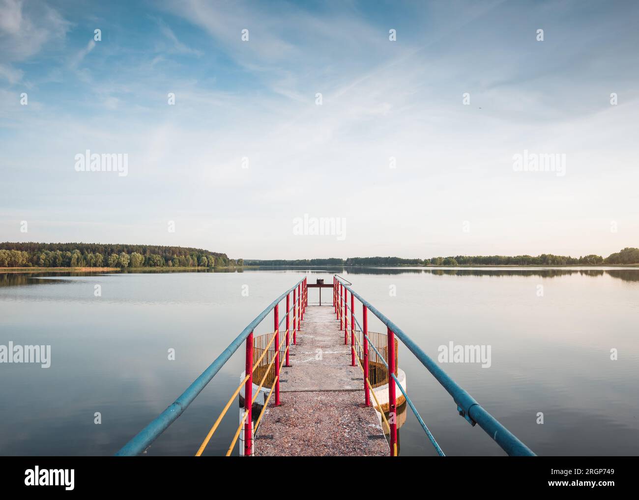 Sommerszene am See: Symmetrisches Foto der Brücke und Reflexion des Waldes im Hintergrund Stockfoto
