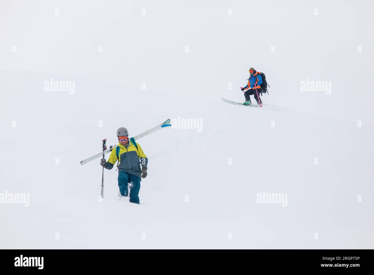 Skifahrer fahren bergab, wenn die Bedingungen für die Schneelandschaft ansteigen Stockfoto