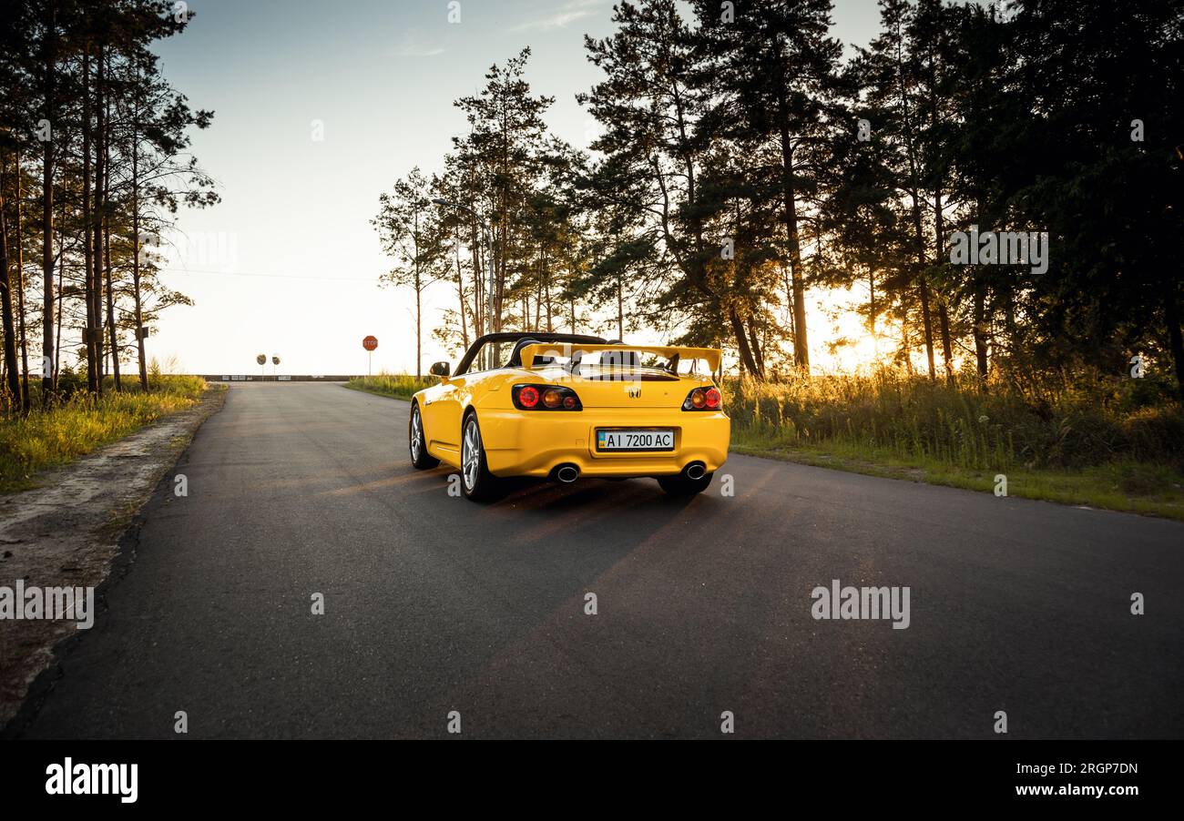 Gelbes Honda S2000 Typ S parkt auf einer Forststraße bergauf. Statische Aufnahme eines japanischen Roadsters bei Sonnenuntergang. Stockfoto