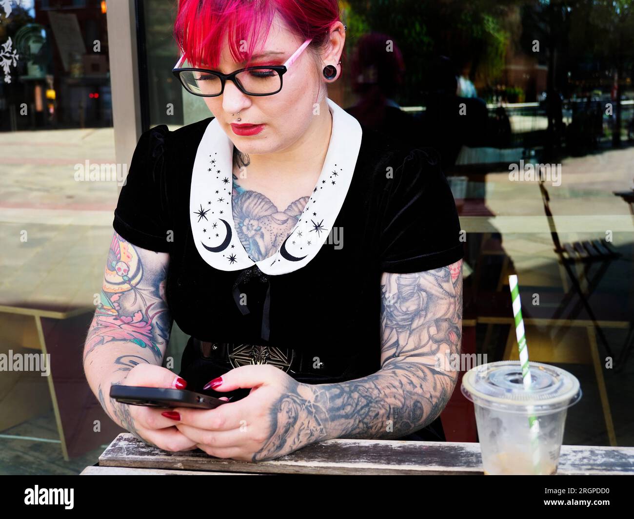 Eine Frau Mitte zwanzig mit gefärbtem rotem Haar und Tätowierungen, die eine Brille mit einem Smartphone trägt, in Leeds West Yorkshire, England Stockfoto