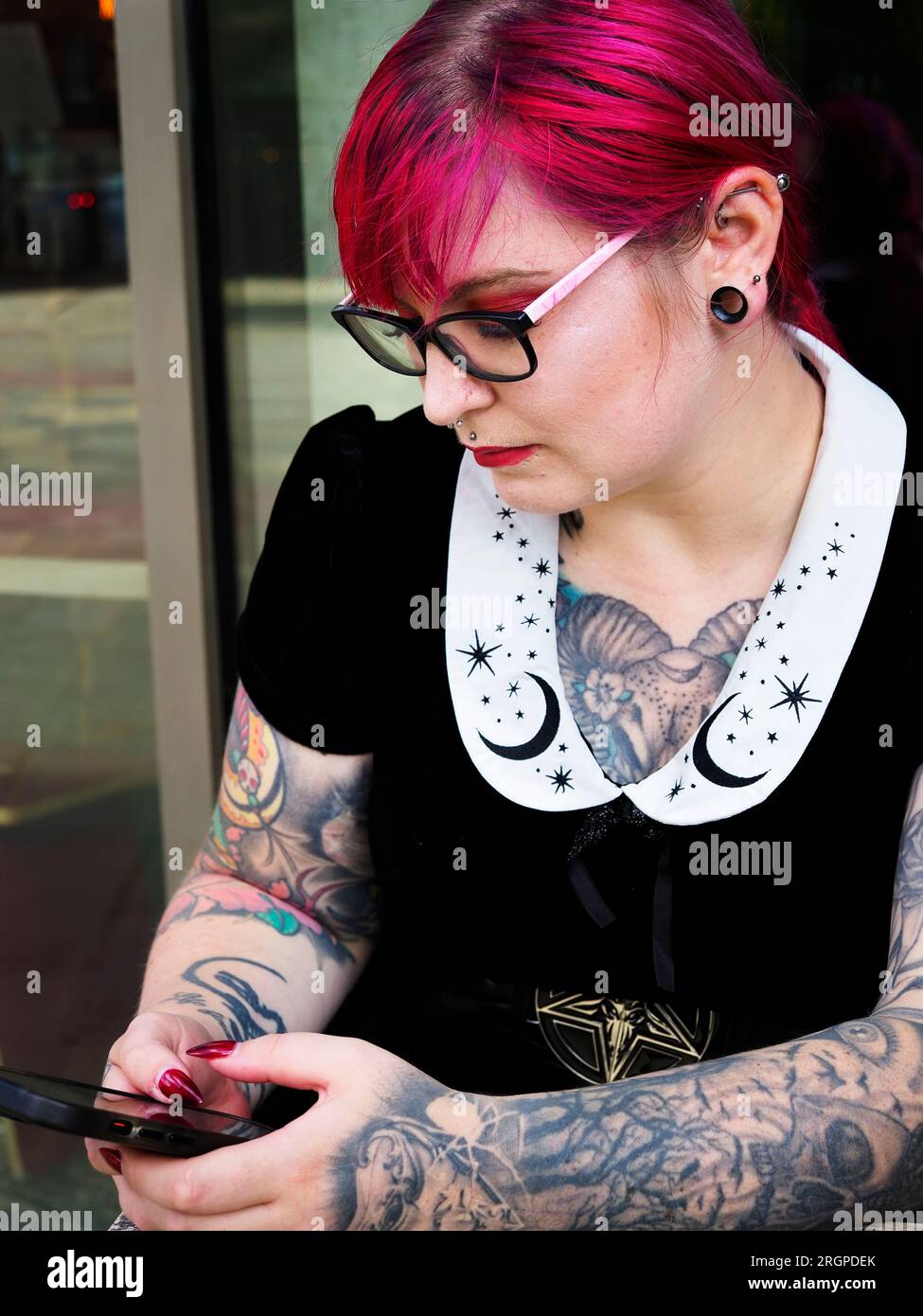 Eine Frau Mitte zwanzig mit gefärbtem rotem Haar und Tätowierungen, die eine Brille mit einem Smartphone trägt, in Leeds West Yorkshire, England Stockfoto