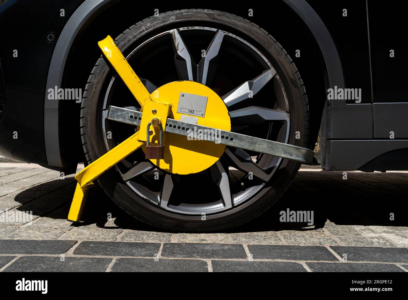 Das Fahrzeugrad wird durch ein gelbes Metallschloss oder eine Klemme blockiert. Verstoß gegen das illegale Parken von Fahrzeugen in einer Sperrzone. Stockfoto