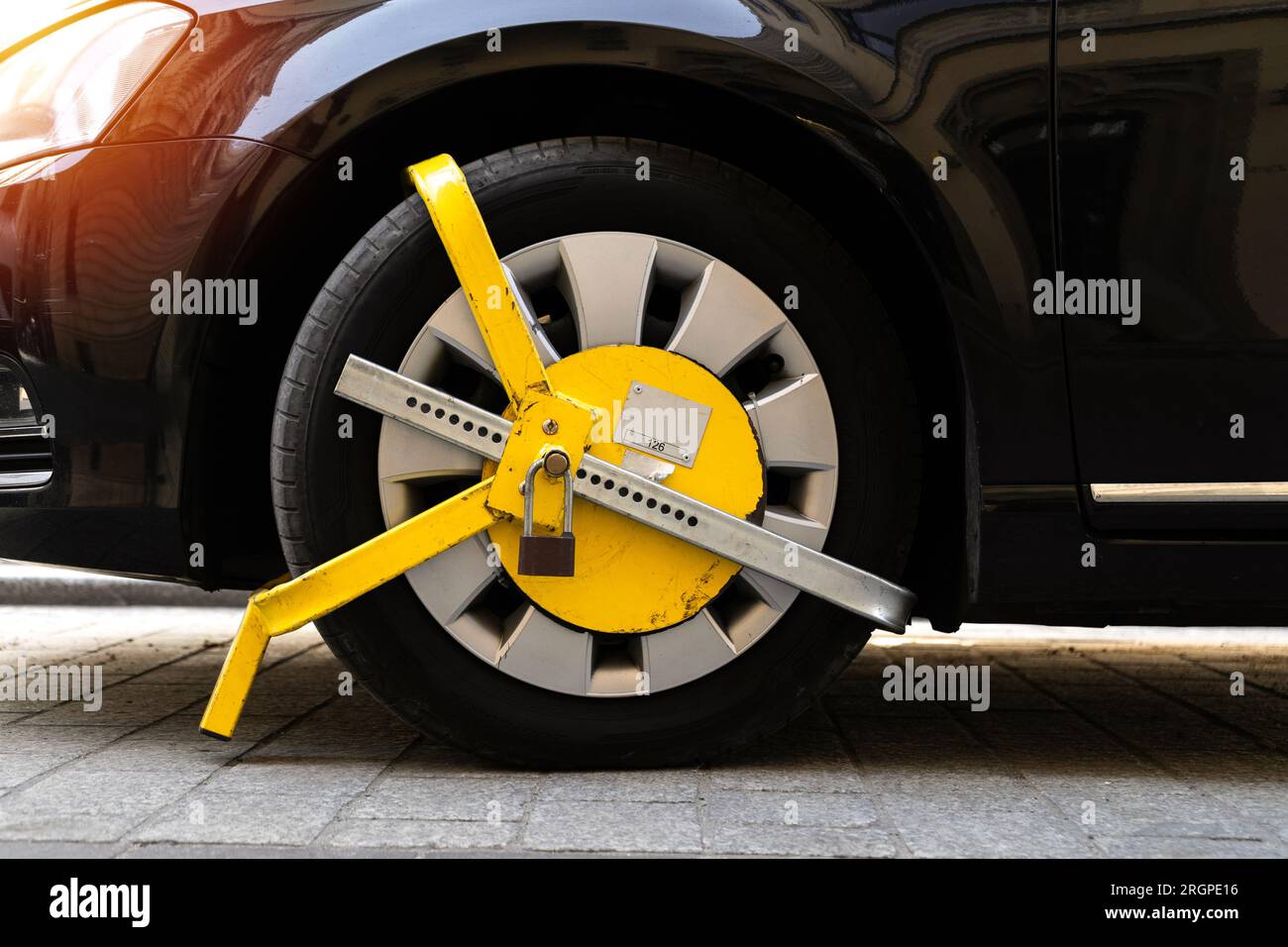 Das Fahrzeugrad wird durch ein gelbes Metallschloss oder eine Klemme blockiert. Verstoß gegen das illegale Parken von Fahrzeugen in einer Sperrzone. Stockfoto