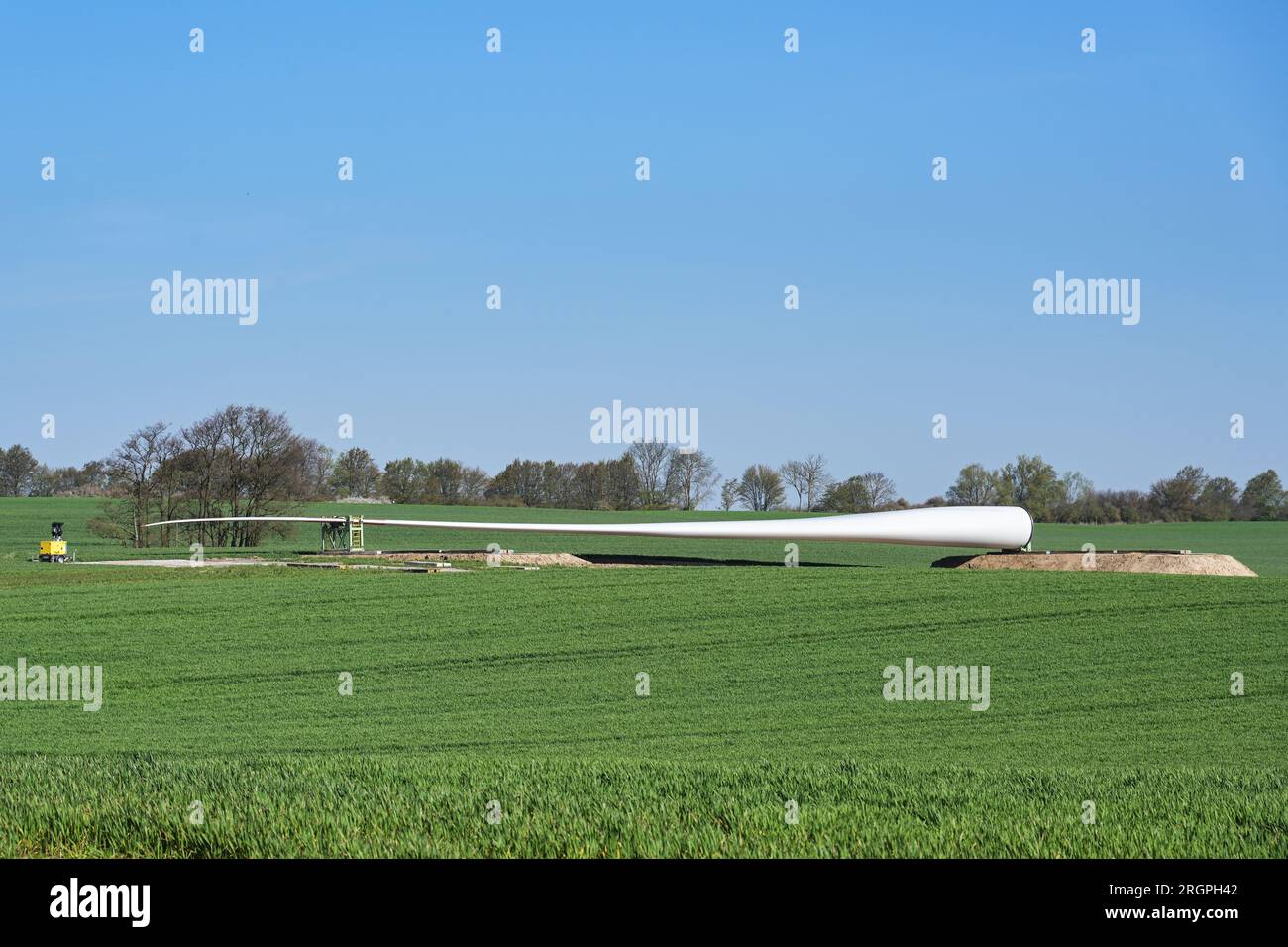 Windturbinenschaufel auf einem landwirtschaftlichen Feld in der Nähe des geplanten Installationsstandorts, Vorbereitung für den Bau eines Kraftwerks für erneuerbare Energien, blu Stockfoto