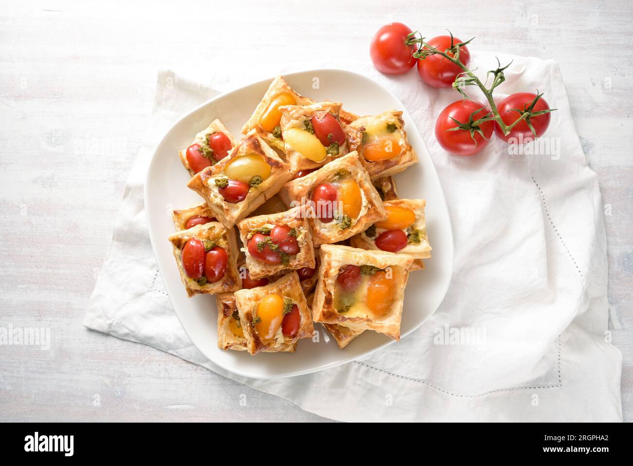 Gebackene Blätterteig-Snacks mit Frischkäse, Tomaten und Kräuterpesto, Partyfinger-Food auf einem weißen Teller, Blick von oben, Kopierraum, Auswahl Stockfoto