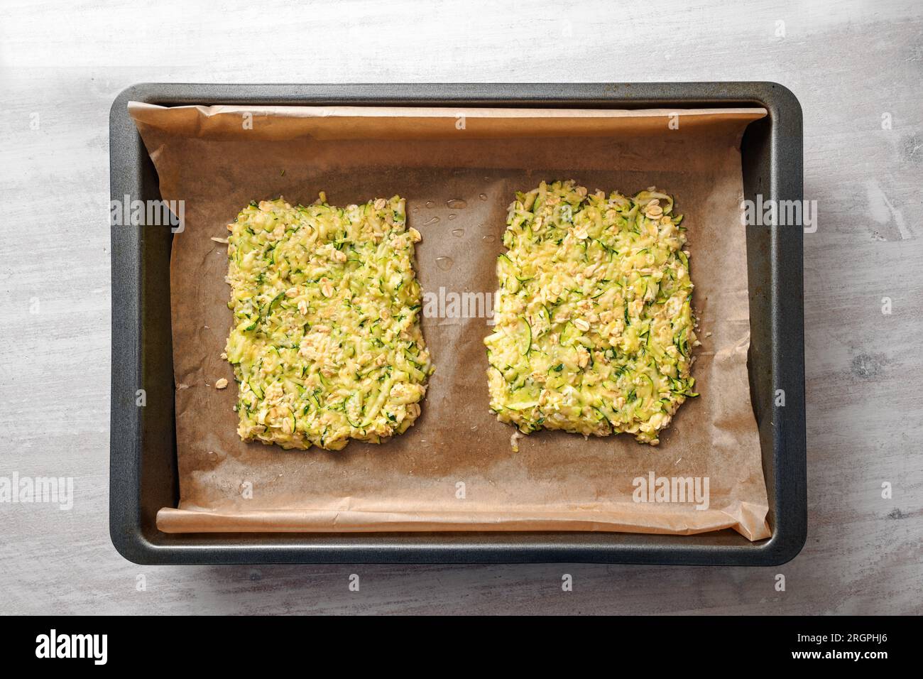 Zucchini- und Haferflocken-Teig als Basis für vegane kohlenhydratarme Pizza oder Gemüsekuchen auf einem Tablett mit Backpapier, hohe Sicht von oben, ausgewählt Stockfoto