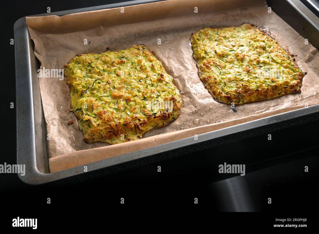 Gebackener Teig aus Zucchini und Haferflocken als Basis für vegane kohlenhydratarme Pizza oder Gemüsekuchen auf einem Tablett mit Backpapier, dunklem Hintergrund, Kopierbereich, Stockfoto