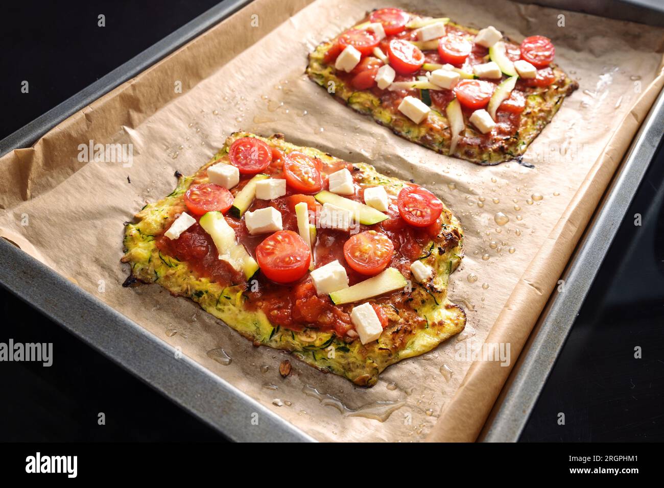 Vegetarische Pizzastücke auf einer Kruste von Zucchini und Haferflocken, garniert mit Tomaten und Fetakäse auf einem Tablett mit Backpapier, gesundes kohlenhydratarmes Ich Stockfoto
