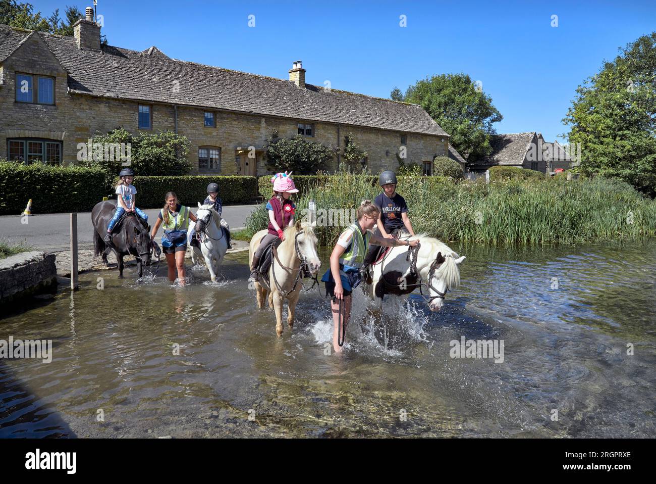 Kinder auf einem Ponyritt durch den Dorfbach bei Lower Slaughter Cotswolds England UK Stockfoto