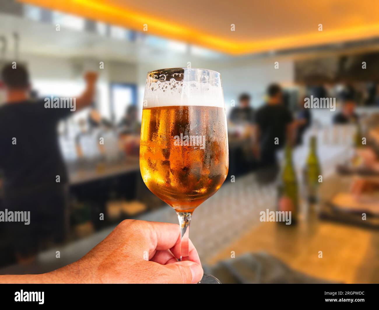 Halten Sie ein Glas schaumiges Bier vom Fass mit verschwommener Restaurantumgebung im Hintergrund. Stockfoto