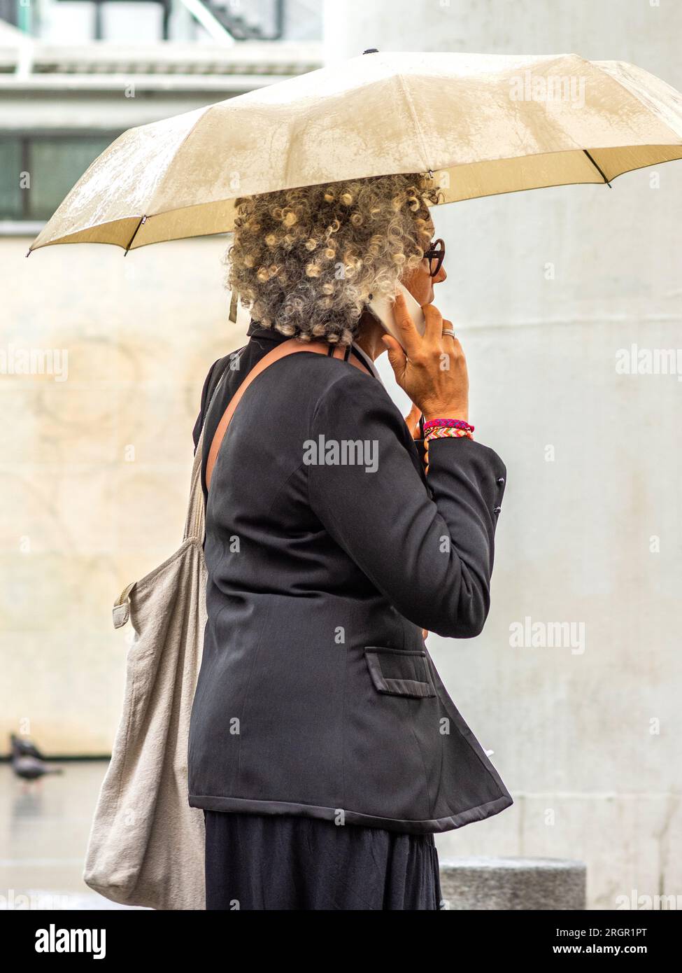 Eine Frau mit Dauerhaar, die einen Regenschirm hält und im regnerischen Paris telefoniert. Stockfoto