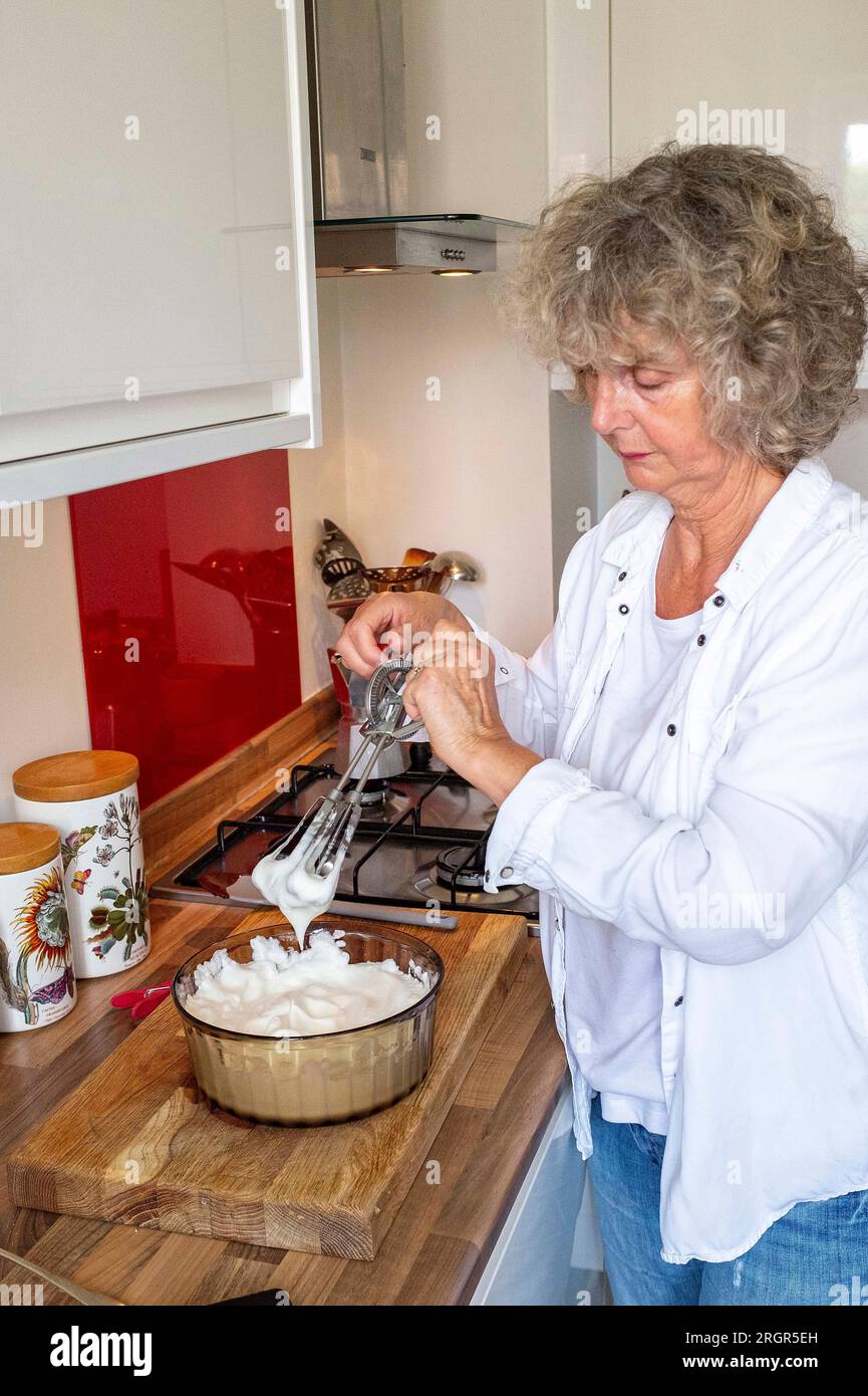 Frau zu Hause kocht Eiweiß mit der Hand zu steifen Gipfeln, um einen Schokoladenmousse oder Baiser zu machen Stockfoto