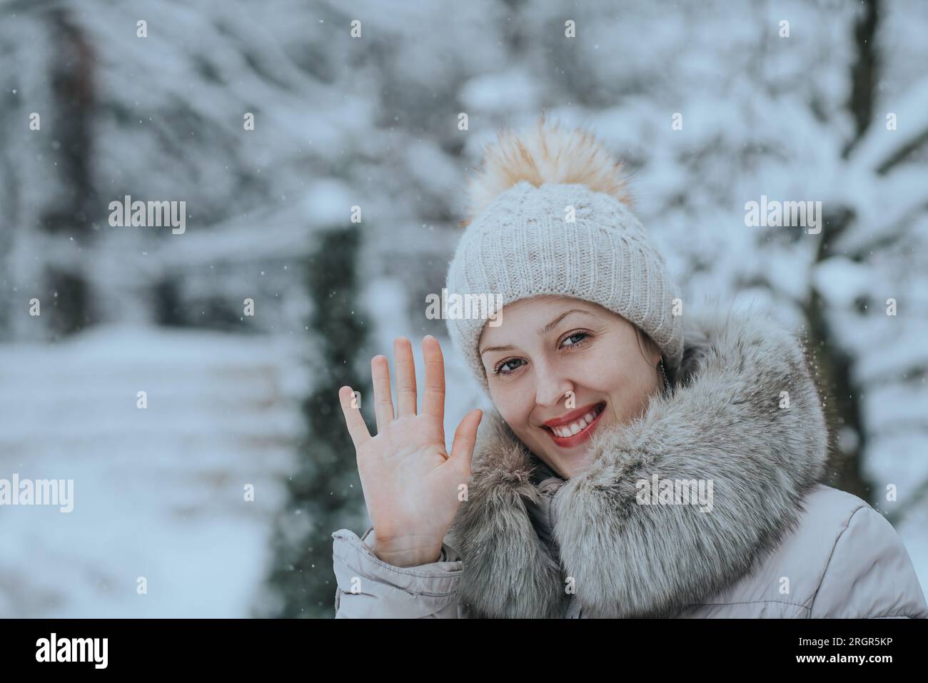 Junge Frau in warmer Winterkleidung, die mit der Hand winkt Stockfoto