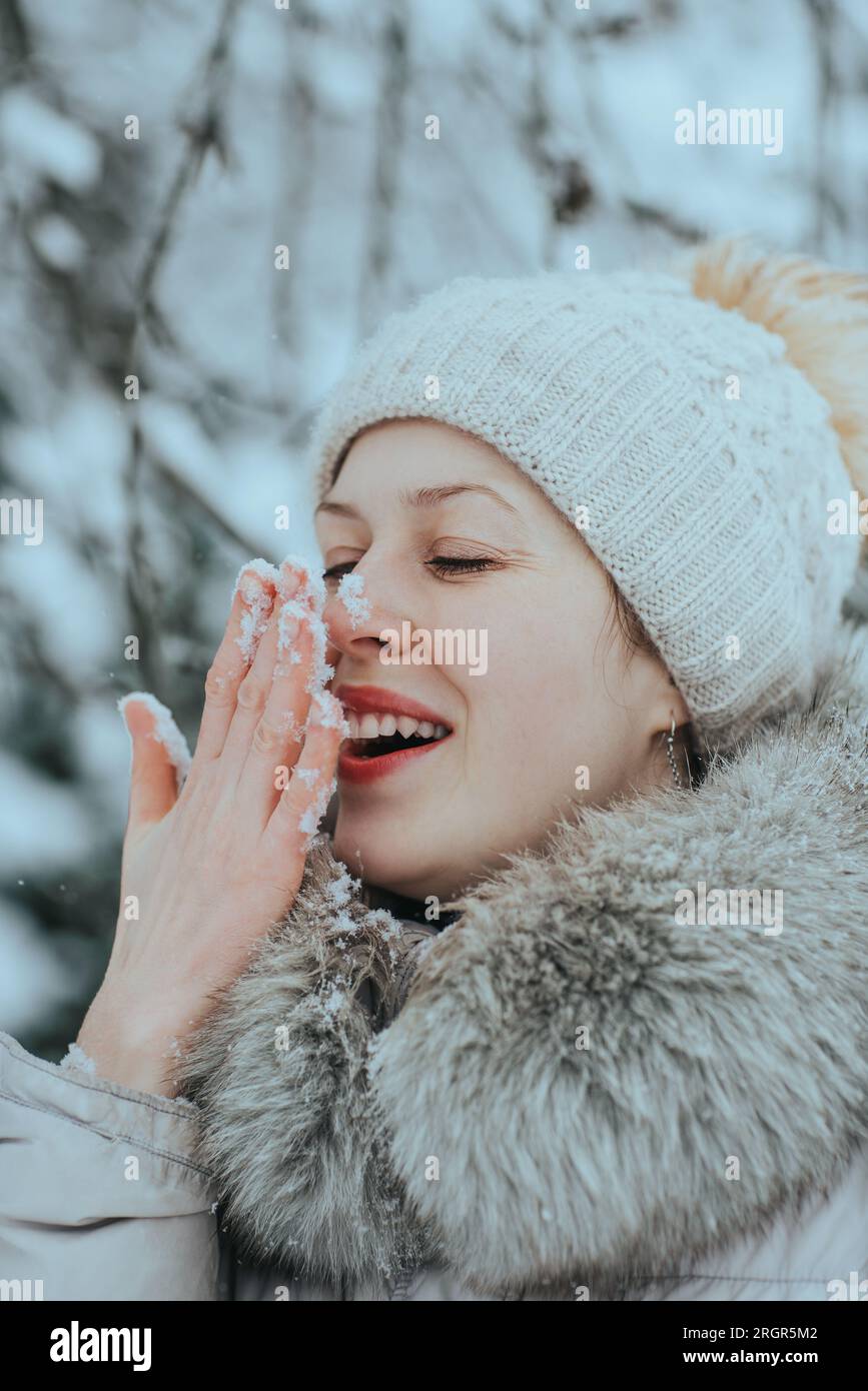Porträt einer jungen glücklichen Frau in warmer Winterkleidung mit Schnee auf der Nase Stockfoto