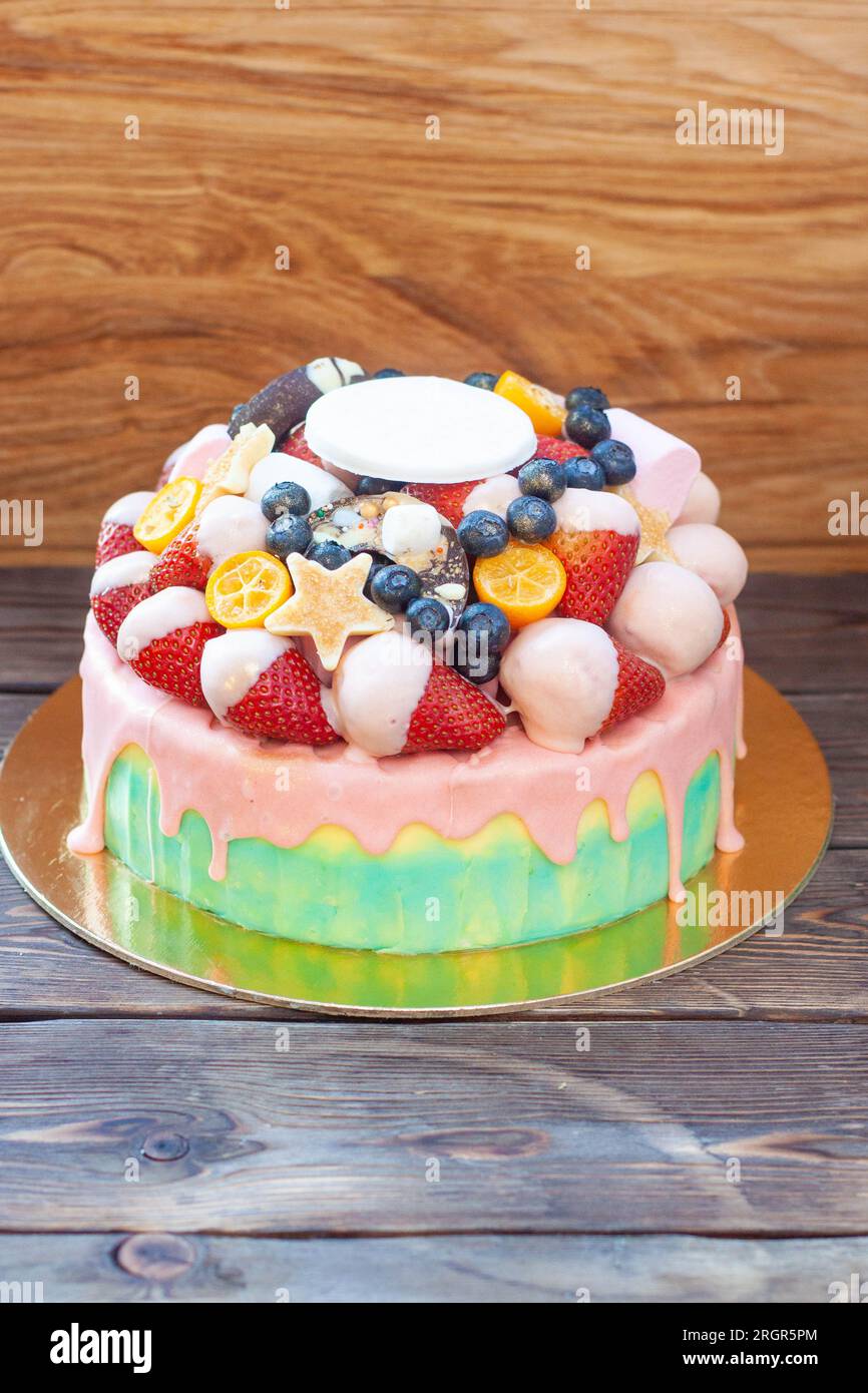 Farbenfroher Kuchen mit Erdbeeren in geschmolzener weißer Schokolade, mit rosafarbener Glasur, frischen Himbeeren, Heidelbeeren und Kumquat Stockfoto