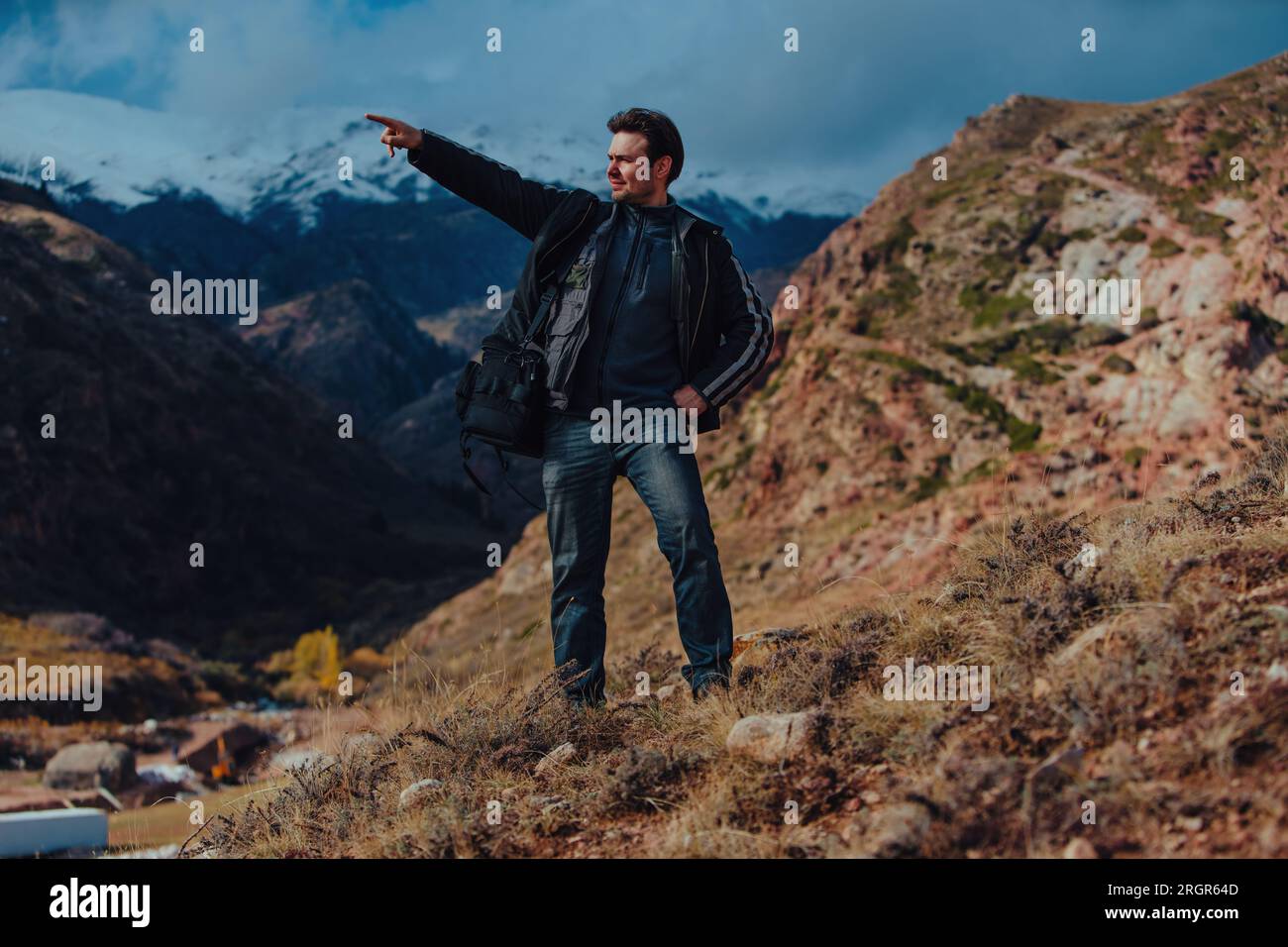 Ein junger Mann mit Tasche steht auf dem Berg und zeigt zur Seite Stockfoto