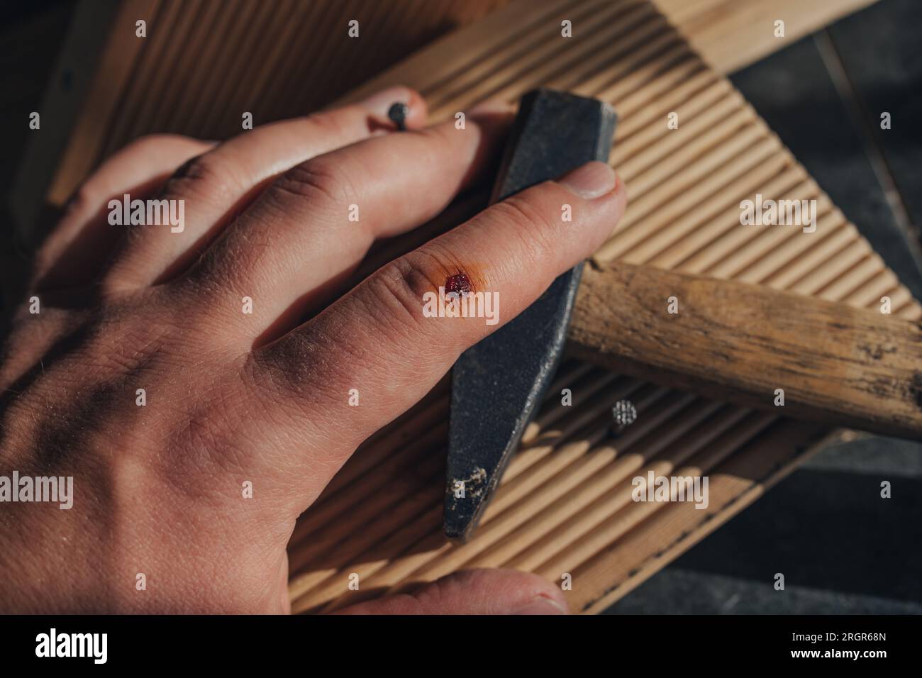 Ein Mann mit verwundetem Arm, der Nägel in ein Holzbrett hämmert Stockfoto