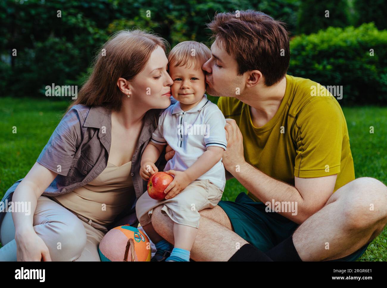Junge Eltern küssen ihr einjähriges Kind im Freien Stockfoto