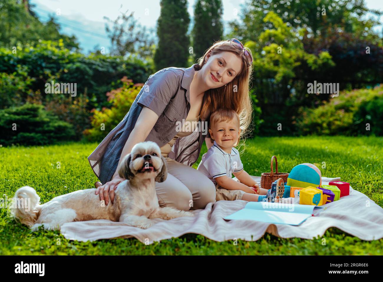 Junge Mutter mit einjährigem Kind und Hund, die im Sommer im Park sitzen Stockfoto