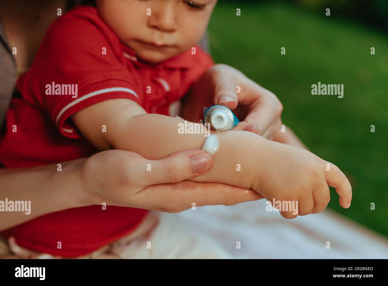 Mutter legt im Sommer Sahne auf die Hand des Babys Stockfoto