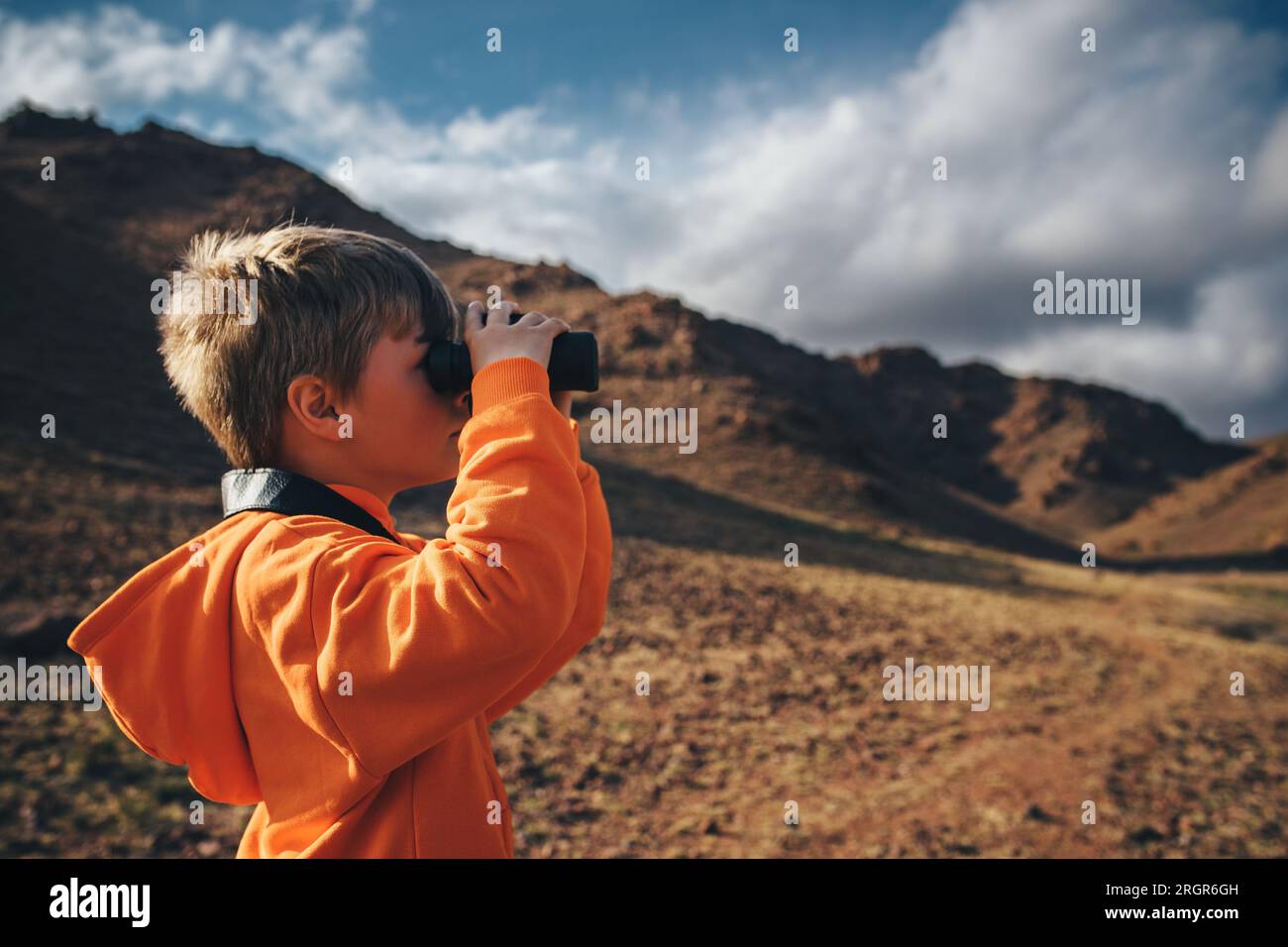 Porträt eines Tourismusjungen, der in einem Fernglas in den Bergen sucht Stockfoto