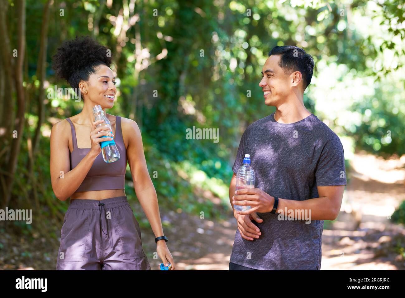 Zwei müde Fitnesspartner trinken Wasser auf Wanderwegen, laufen durch den Wald, trainieren Stockfoto