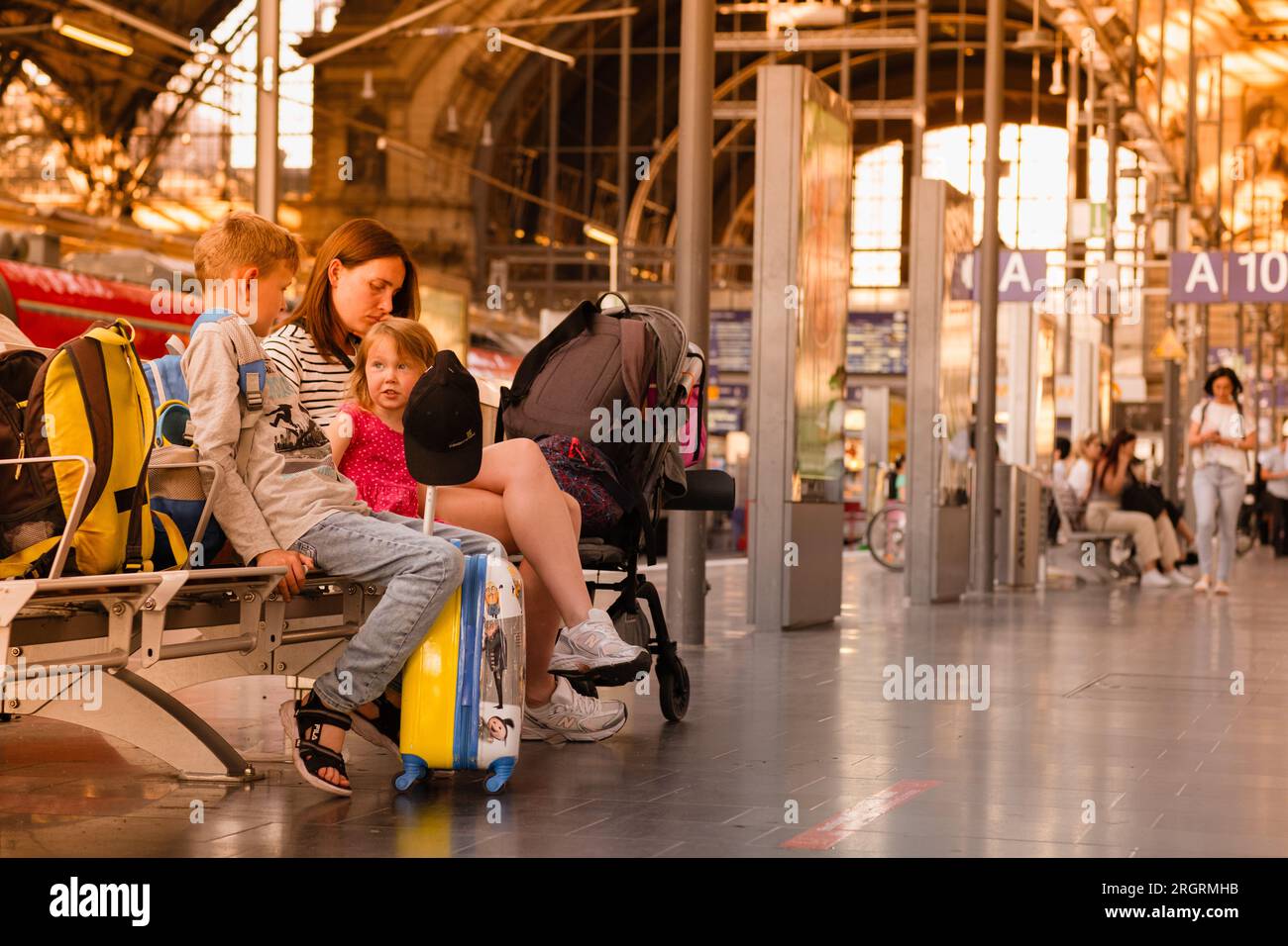 Die Familie am Bahnhof wartet auf den Zug, umgeben von Gepäck. Mom und Kinder sitzen auf der Bank des Bahnhofs und warten auf die Tr Stockfoto