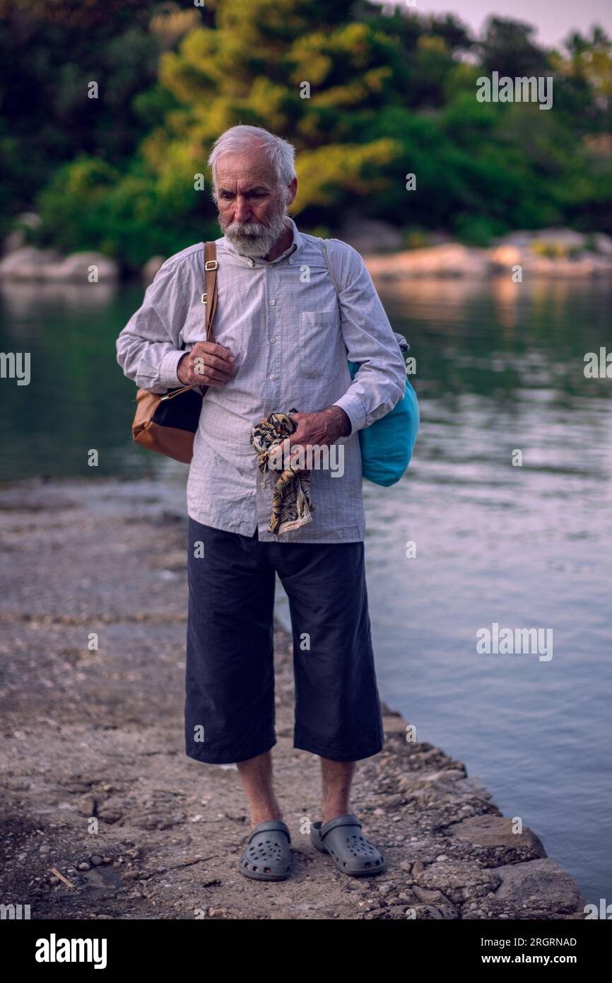 Ein alter Mann mit Bart steht am Meer. Ein älterer Mann reist. Ein alter Mann geht am Meer entlang. Stockfoto