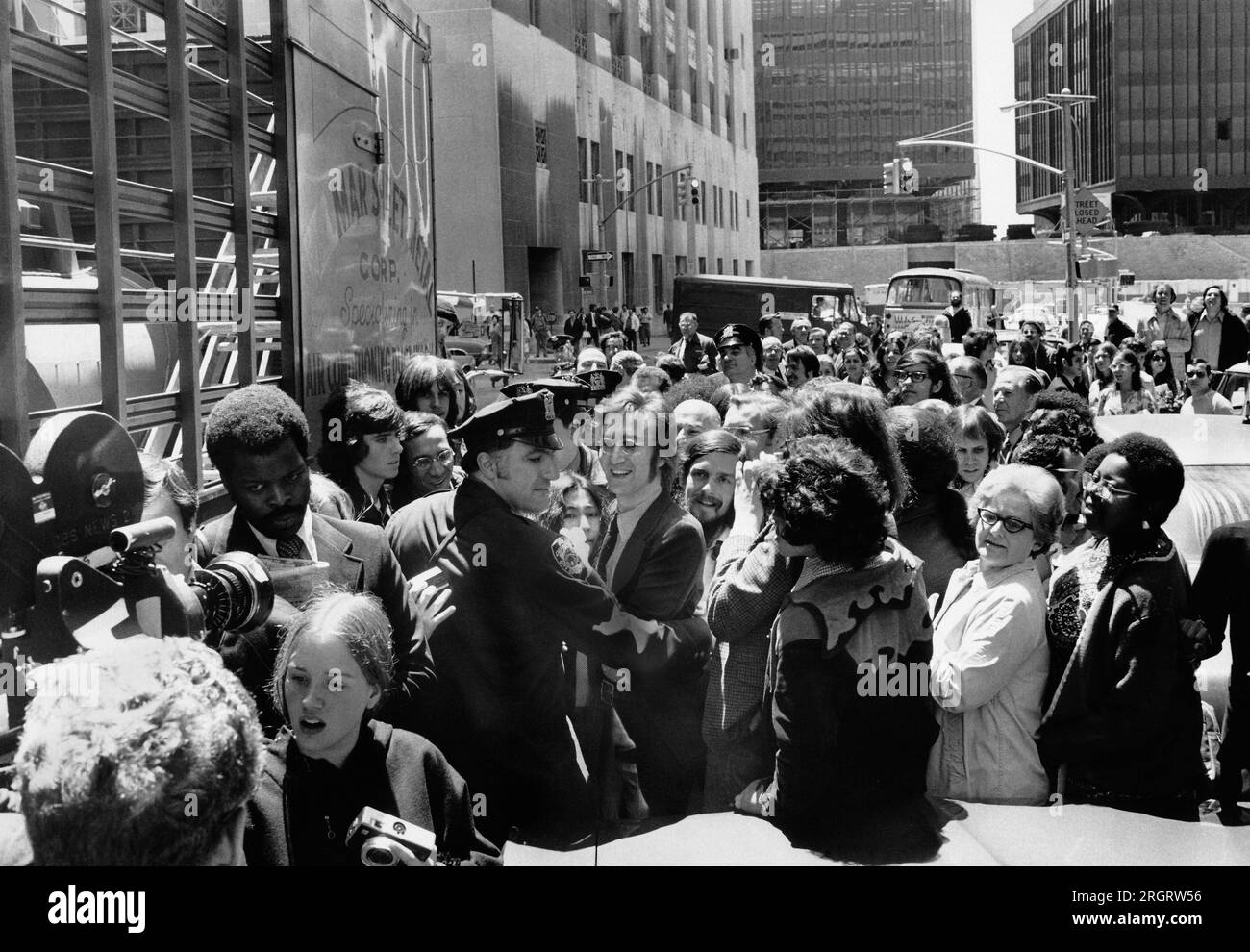 New York, New York: Am 12. Mai 1972 werden John Lennon und Yoko Ono von einem Polizisten unterstützt, der versucht, sich durch die Menge zu arbeiten, nachdem er das Einwanderungsamt am Broadway verlassen hat. Stockfoto