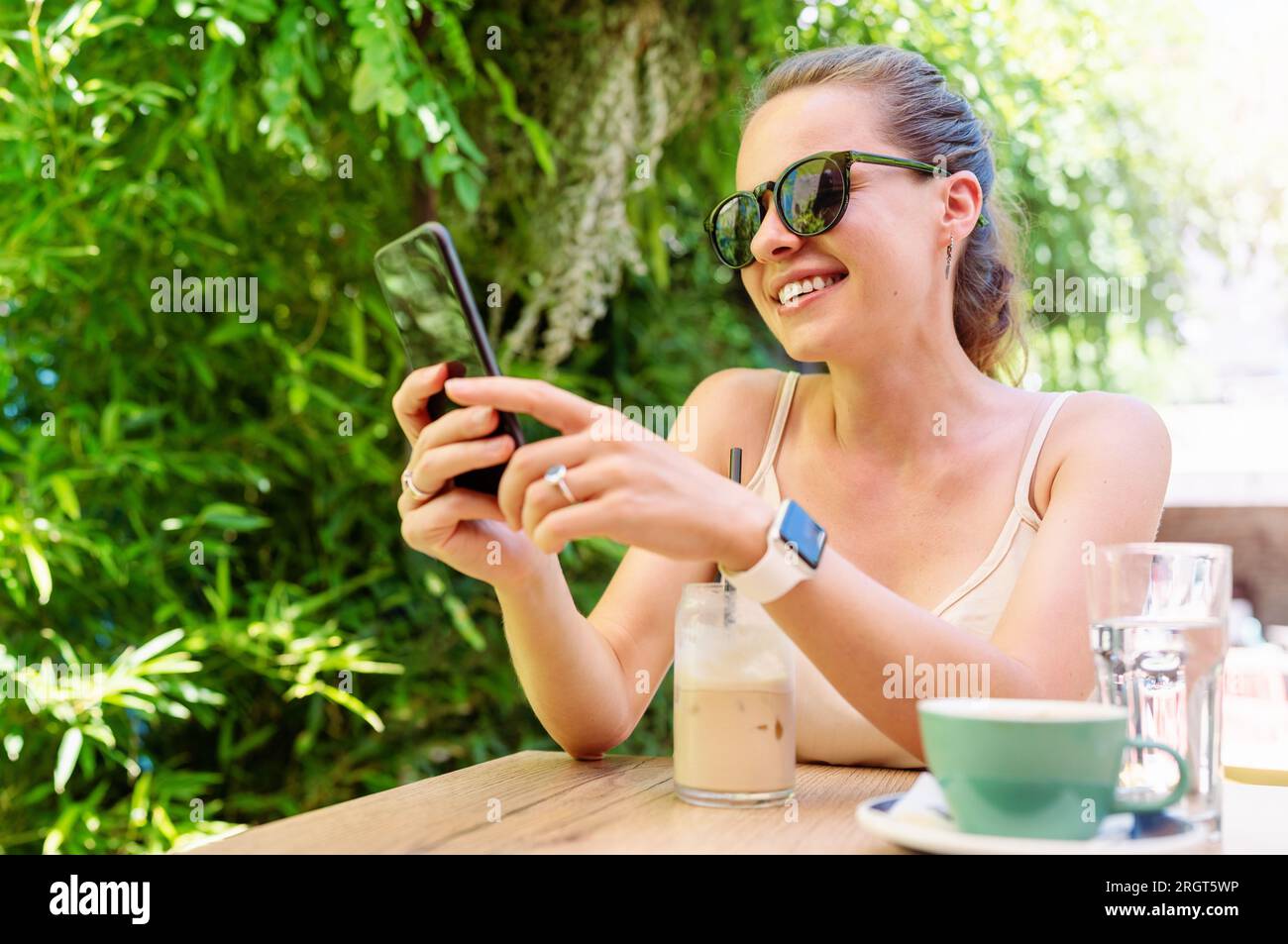 Online-Messaging und -Kommunikation im Lifestyle an öffentlichen Orten, junge moderne Frau trägt eine Sonnenbrille mit Mobiltelefon, während sie im Straßencafé sitzt Stockfoto