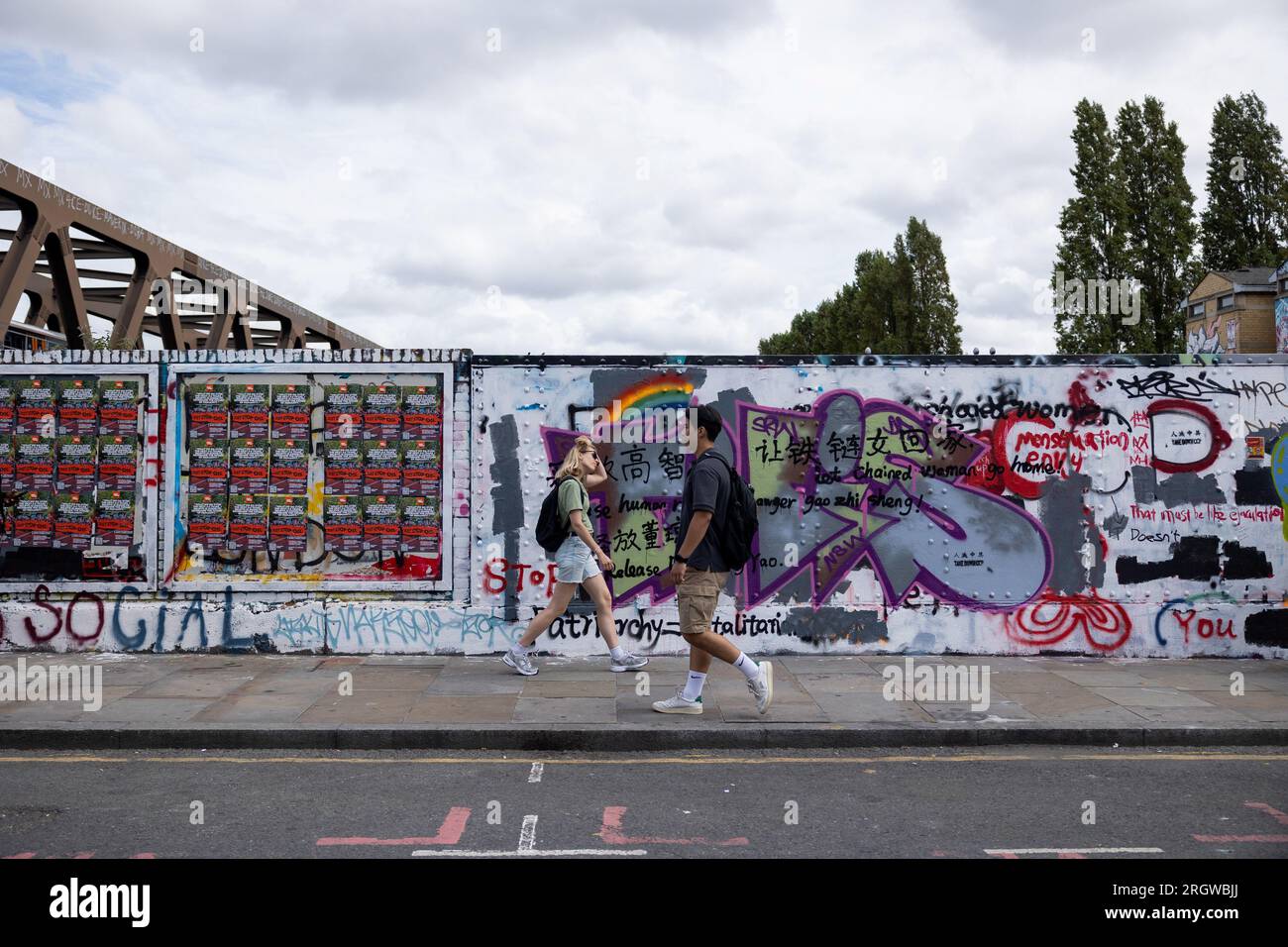 Man sieht Menschen an einer Mauer laufen, die vom Rat der Tower Hamlets umgemalt wurde, aber immer noch mit antichinesischen Parolen in der Brick Lane. Am 5. August bemalte das Royal College of Arts (RCA) die Wand weiß und bedeckte alle bestehenden Graffiti mit den 12 Kernwerten des Sozialismus während der Kulturrevolution, was eine hitzige Debatte zwischen lokalen Künstlern und chinesischen Gemeinschaften anlöste und die Verbreitung prochinesischer Propaganda in Frage stellte. Seit dem 8. August hat der Rat von Tower Hamlets eine Erklärung veröffentlicht, in der die Menschen aufgefordert werden, mit dem Malen weiterer illegaler Graffiti an der Wand aufzuhören Stockfoto