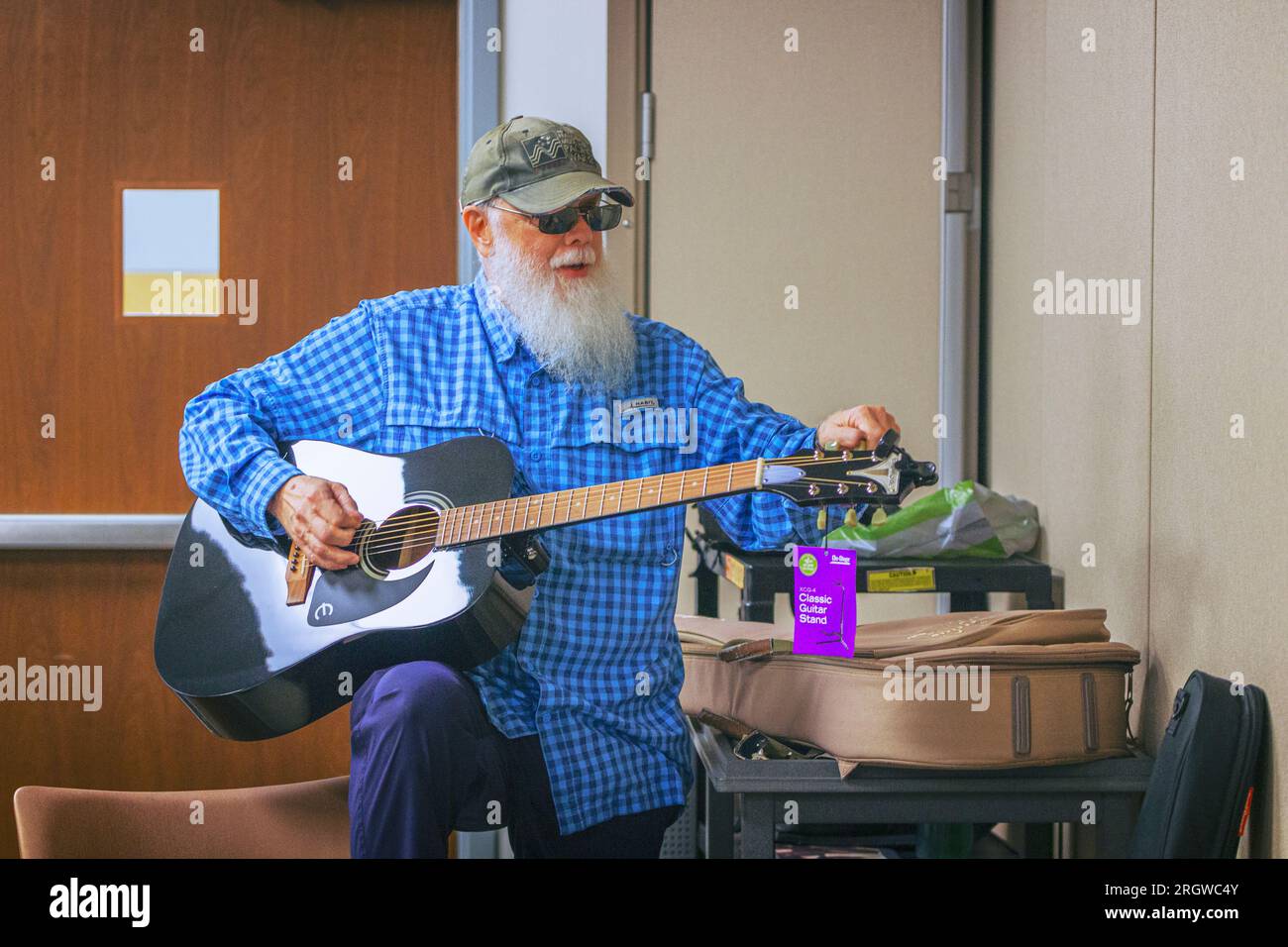 Ein inspirierendes Bild von Pat O'Neill, wie er eine Gitarre in Vorbereitung auf eine Gruppenvorstellung bei der Graduationszeremonie „Gitarren für Vets“ im L-Gebäude sorgfältig tunt Stockfoto