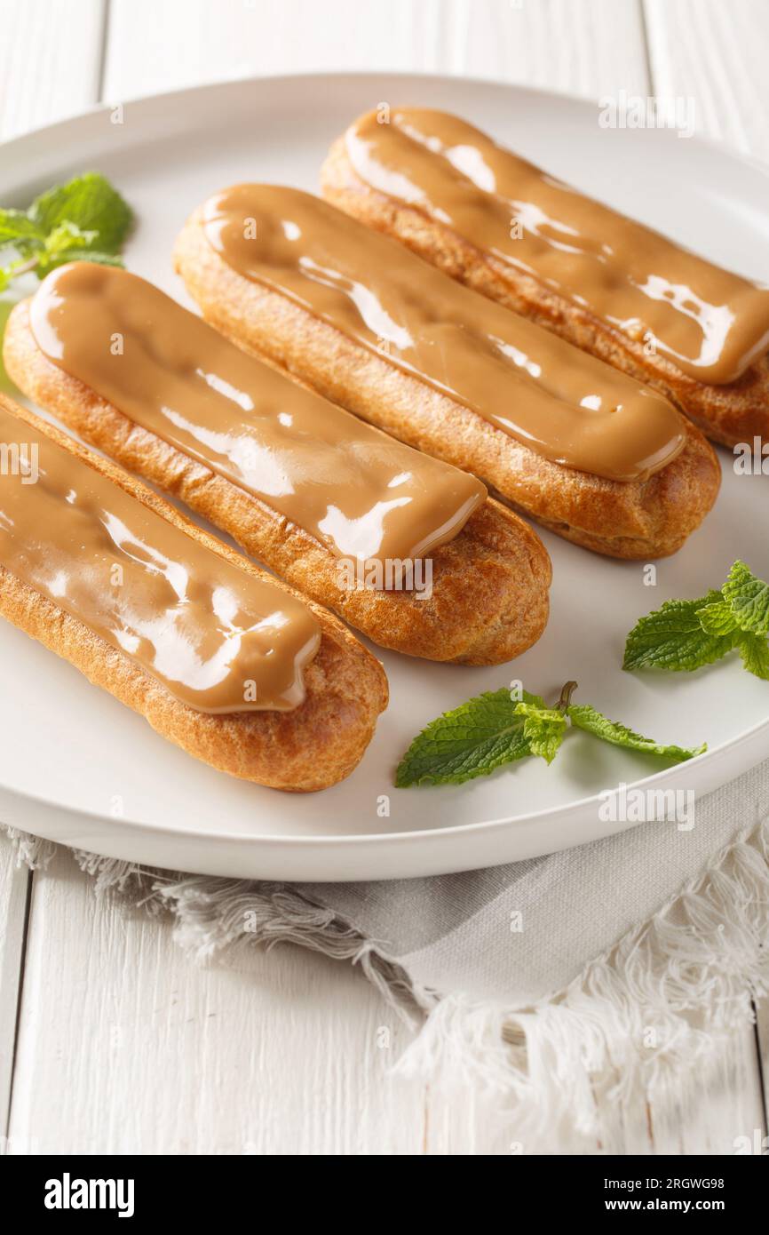 Traditionelle französische Eclairs gefüllt mit Kaffeesahne Nahaufnahme auf einem Teller auf dem Tisch. Vertikal Stockfoto