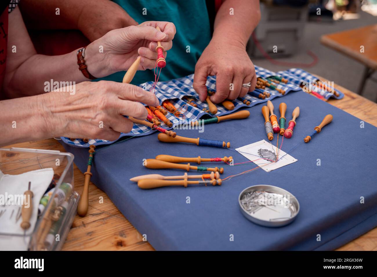 Hände von Menschen, die Spulenspitzen vorbereiten und herstellen. Farbenfrohe Spitzenfäden. Freizeitaktivität. Stockfoto