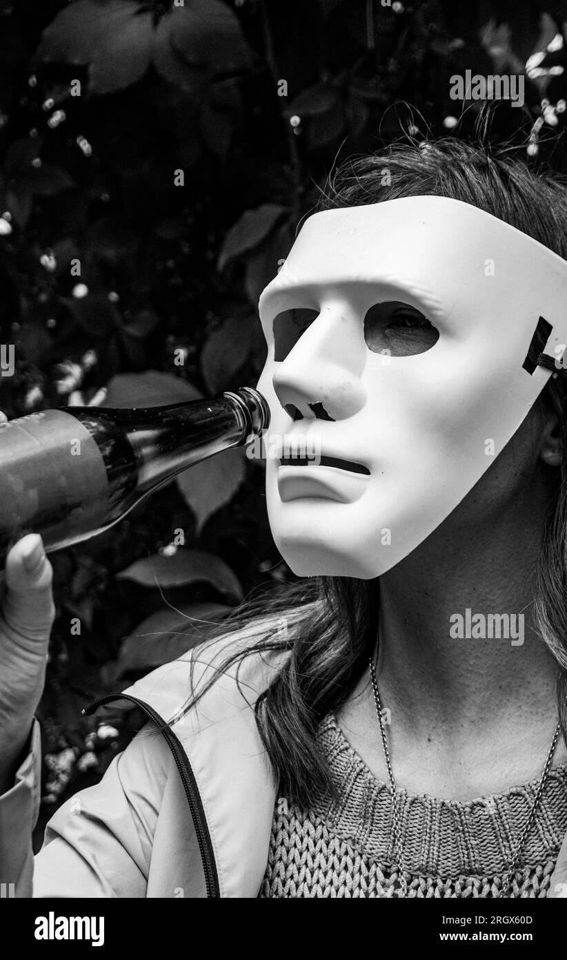 Eine Person, die eine Maske trägt und Bier trinkt Stockfoto