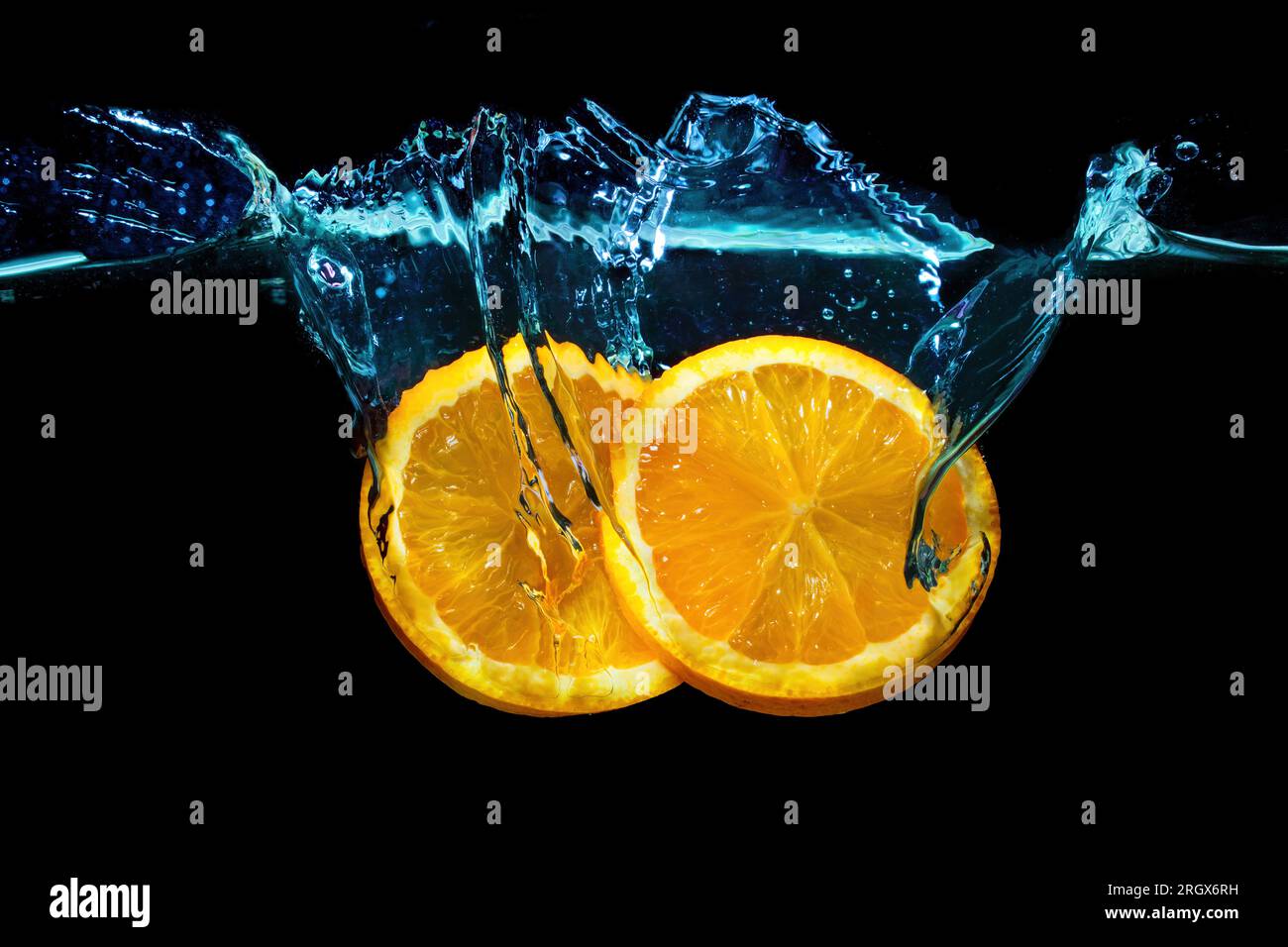 Erfrischende Freude an Zitrusfrüchten: Halbierte Orange taucht anmutig in Wasser ein und sorgt für Spritzer vor schwarzer Kulisse. Stockfoto