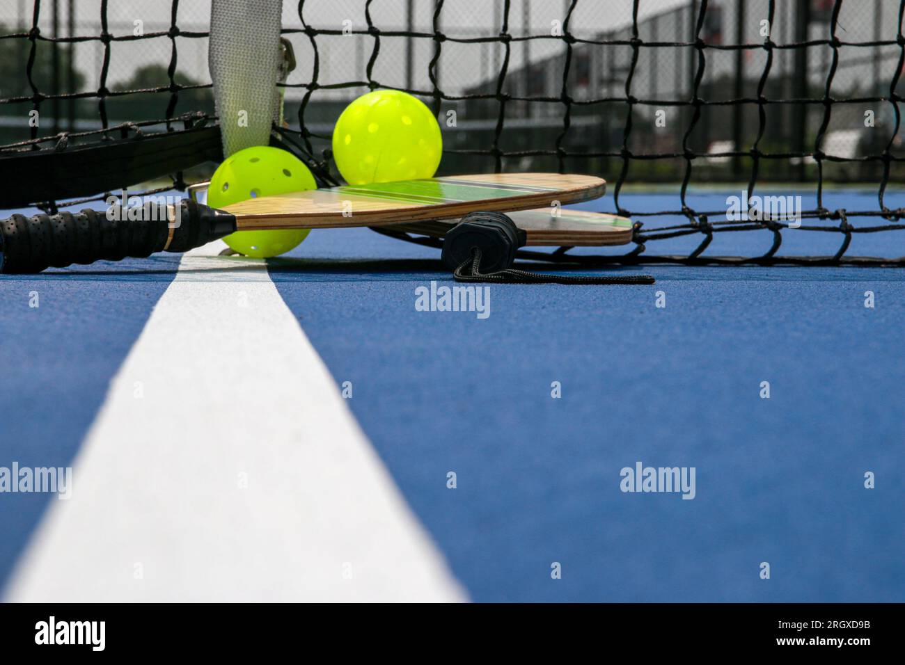 Pickleball paddelt und zwei gelbe Peitschen auf einem blauen Platz auf einer weißen Linie. Stockfoto